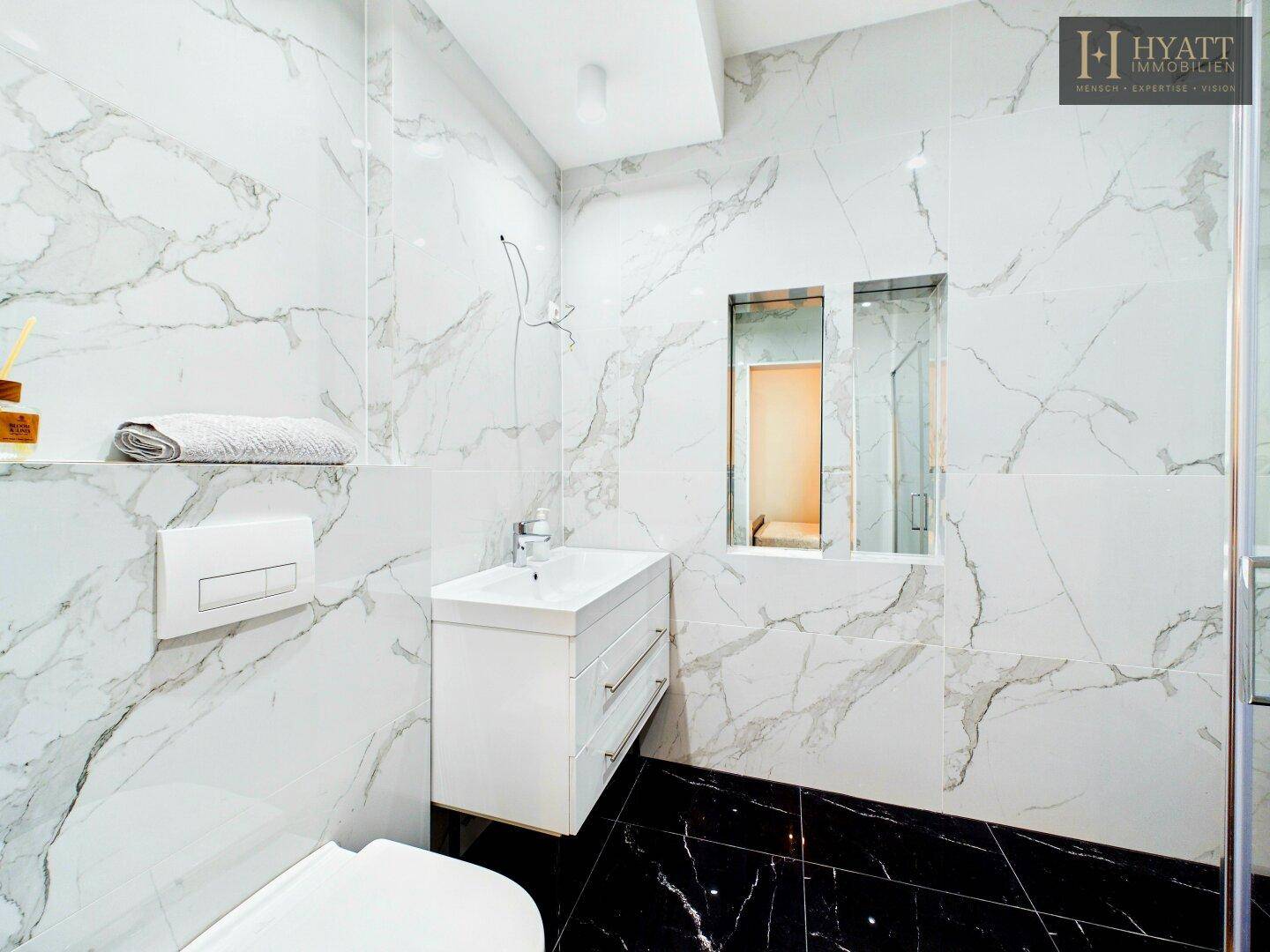 Elegantes Badezimmer mit Marmorwänden, schwarzem Boden und modernem Waschtisch.