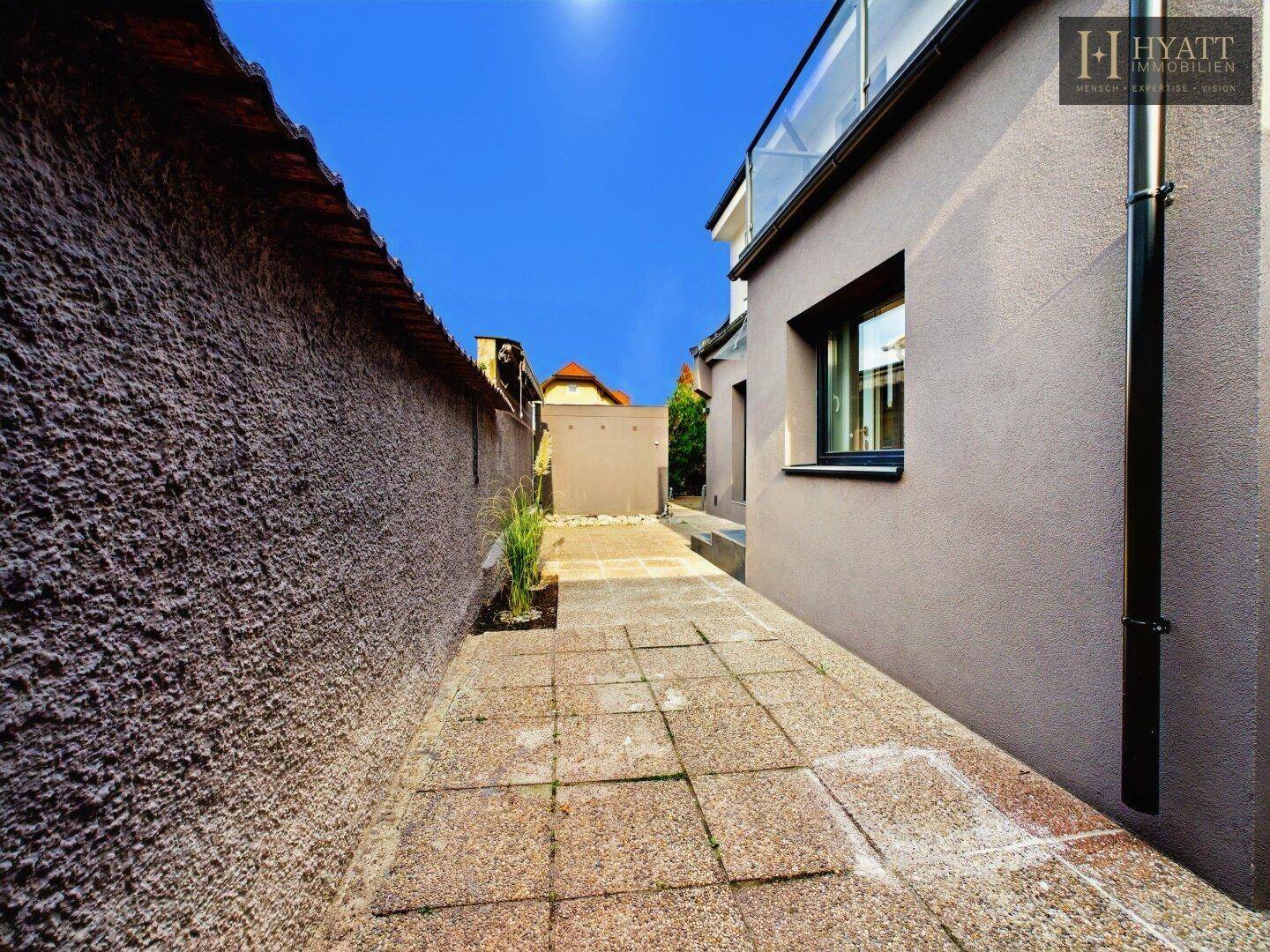 Schmaler gepflasterter Weg zwischen zwei Gebäuden unter strahlend blauem Himmel.