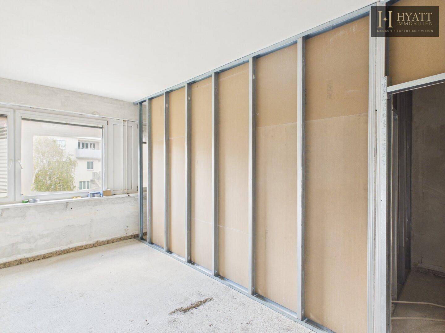 Innenraum im Rohbau mit Trockenbauwänden und Fensterblick nach draußen, wartet auf den Ausbau.