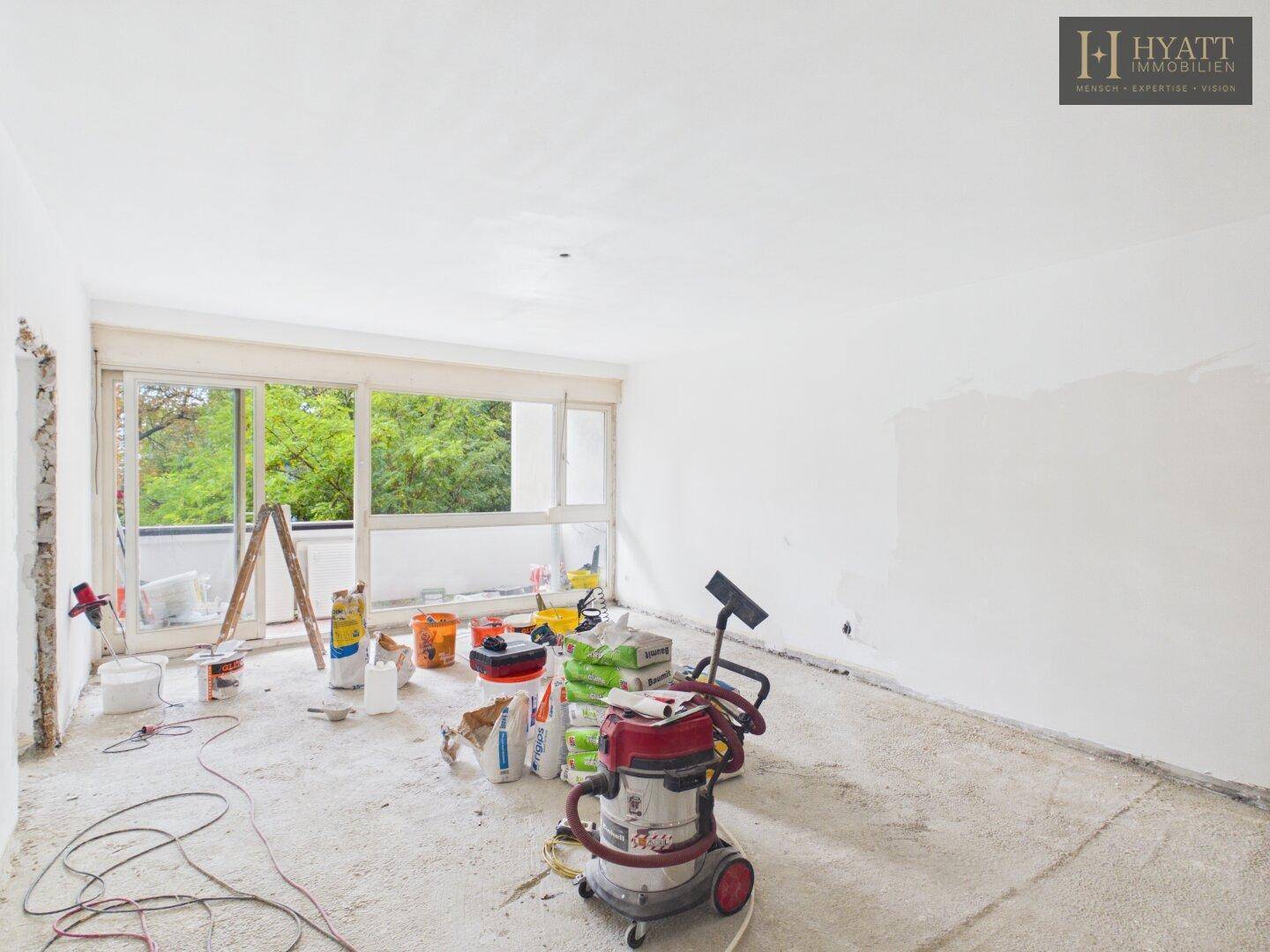 Geräumiges Wohnzimmer im Rohbau mit großen Fenstern und Zugang zum Balkon, lichtdurchflutet.