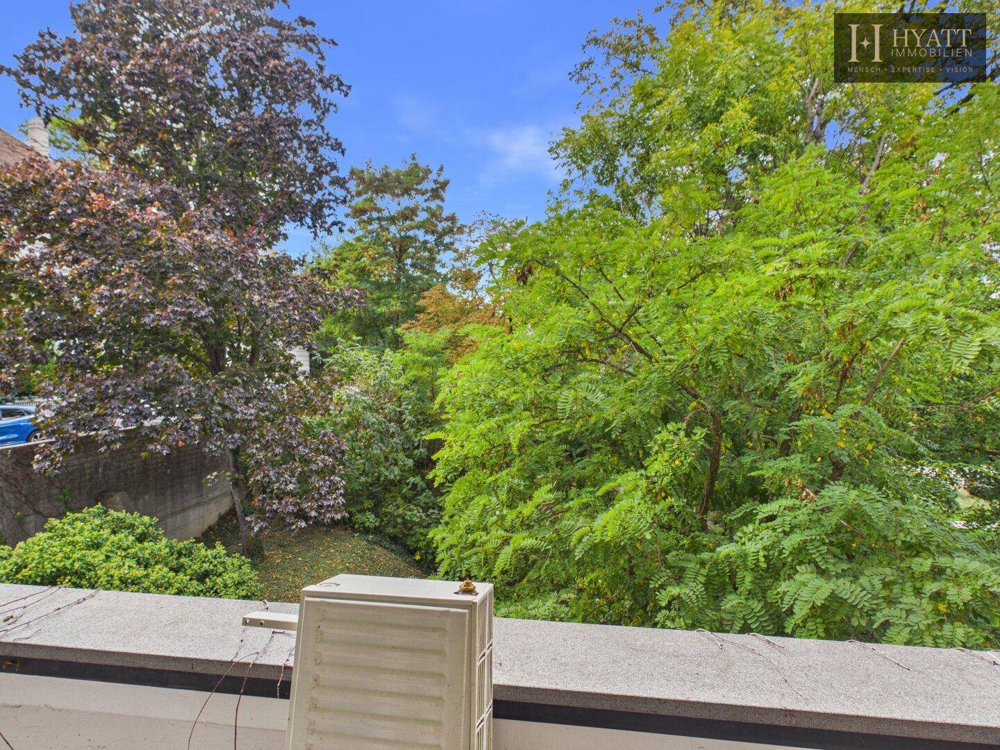 Blick vom Balkon ins Grüne mit üppigen Bäumen und Sträuchern, bietet eine ruhige Aussicht.