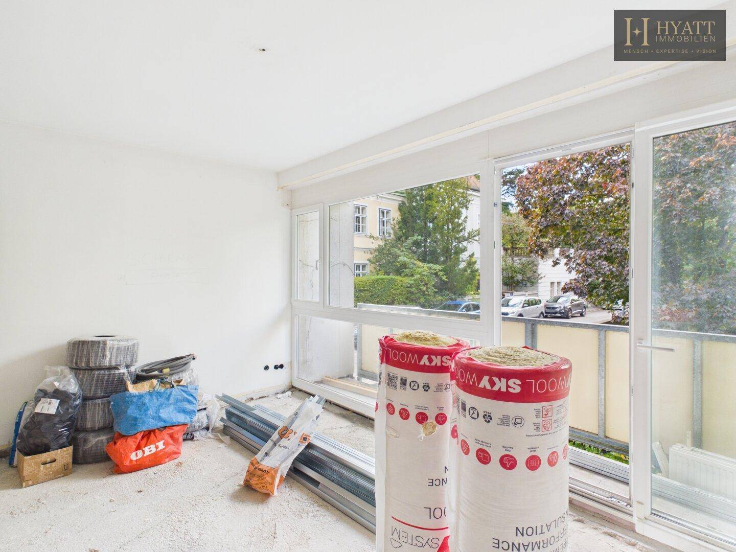 Raum im Rohbau mit Isolationsmaterialien und Blick auf die Straße durch große Fenster, bereit für den Ausbau.