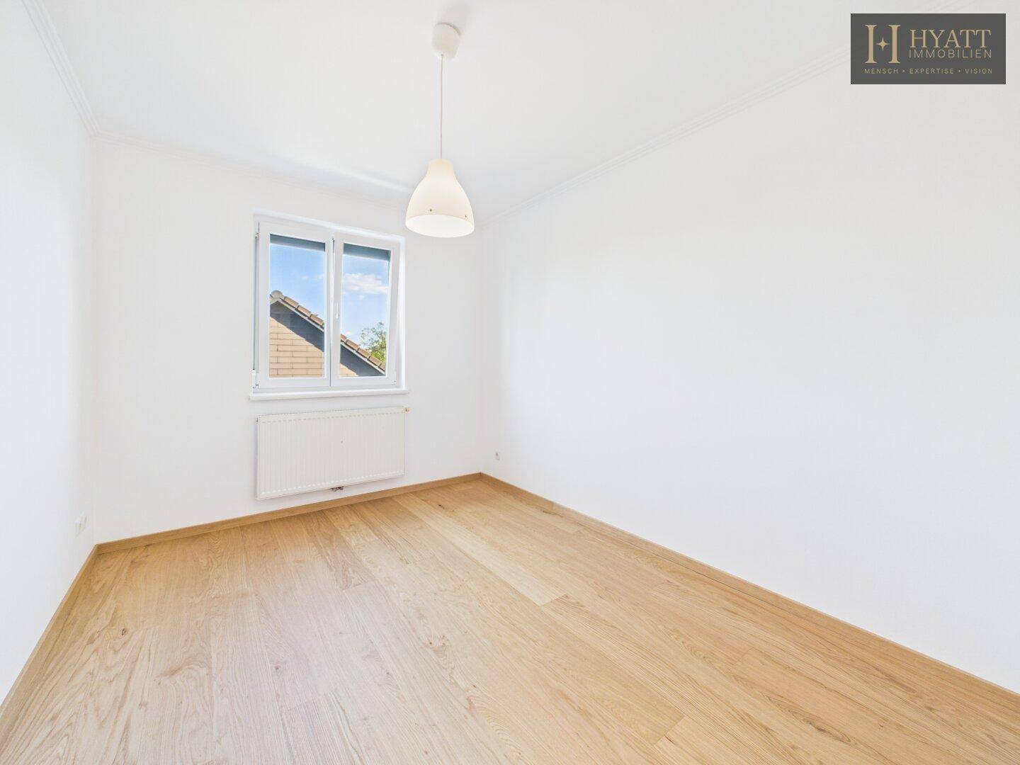 Helles Schlafzimmer mit Holzboden, weiß gestrichenen Wänden und Fenster.