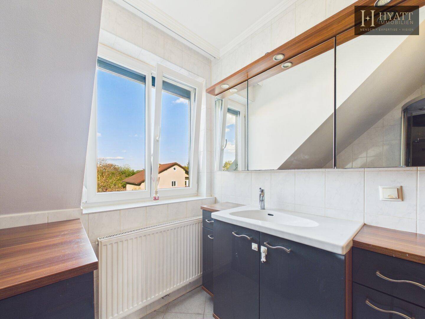 Badezimmer mit Waschbecken, Spiegelschrank, Fenster und Dachschräge.