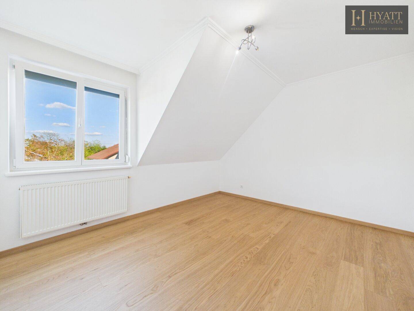 Helles Schlafzimmer mit Holzboden, weißen Wänden und Fenster unter der Dachschräge.