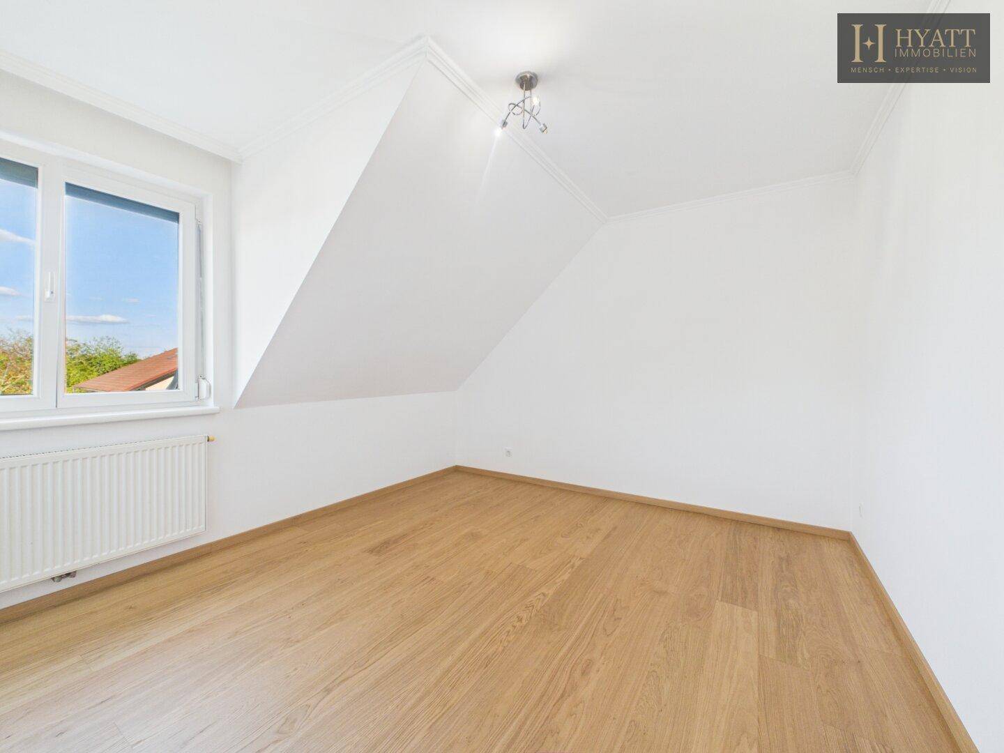 Freundliches Schlafzimmer mit Holzboden, weißen Wänden und Fenster.