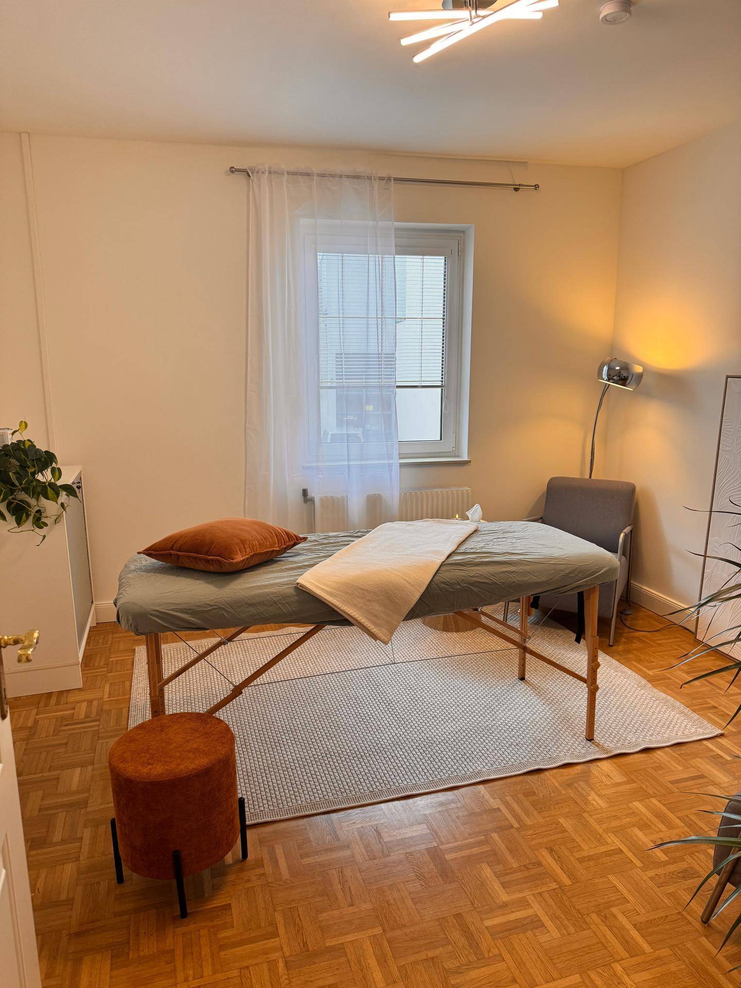 Heller Behandlungsraum mit Massageliege, einem Sessel und Parkettboden.