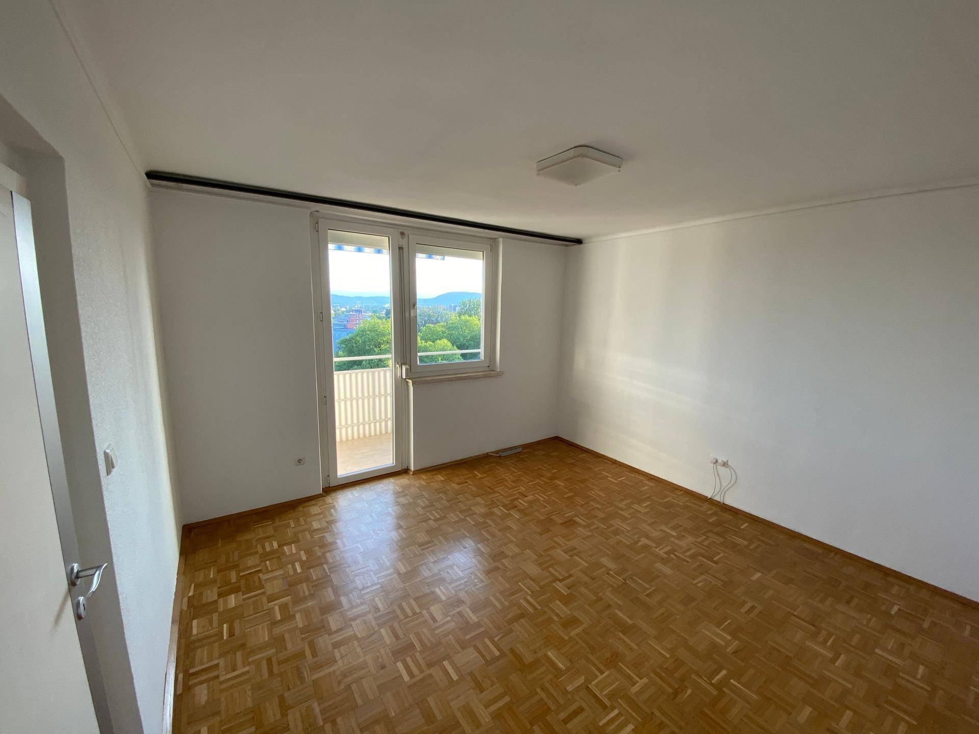 Helles Schlafzimmer mit Parkettboden und direktem Zugang zum Balkon.