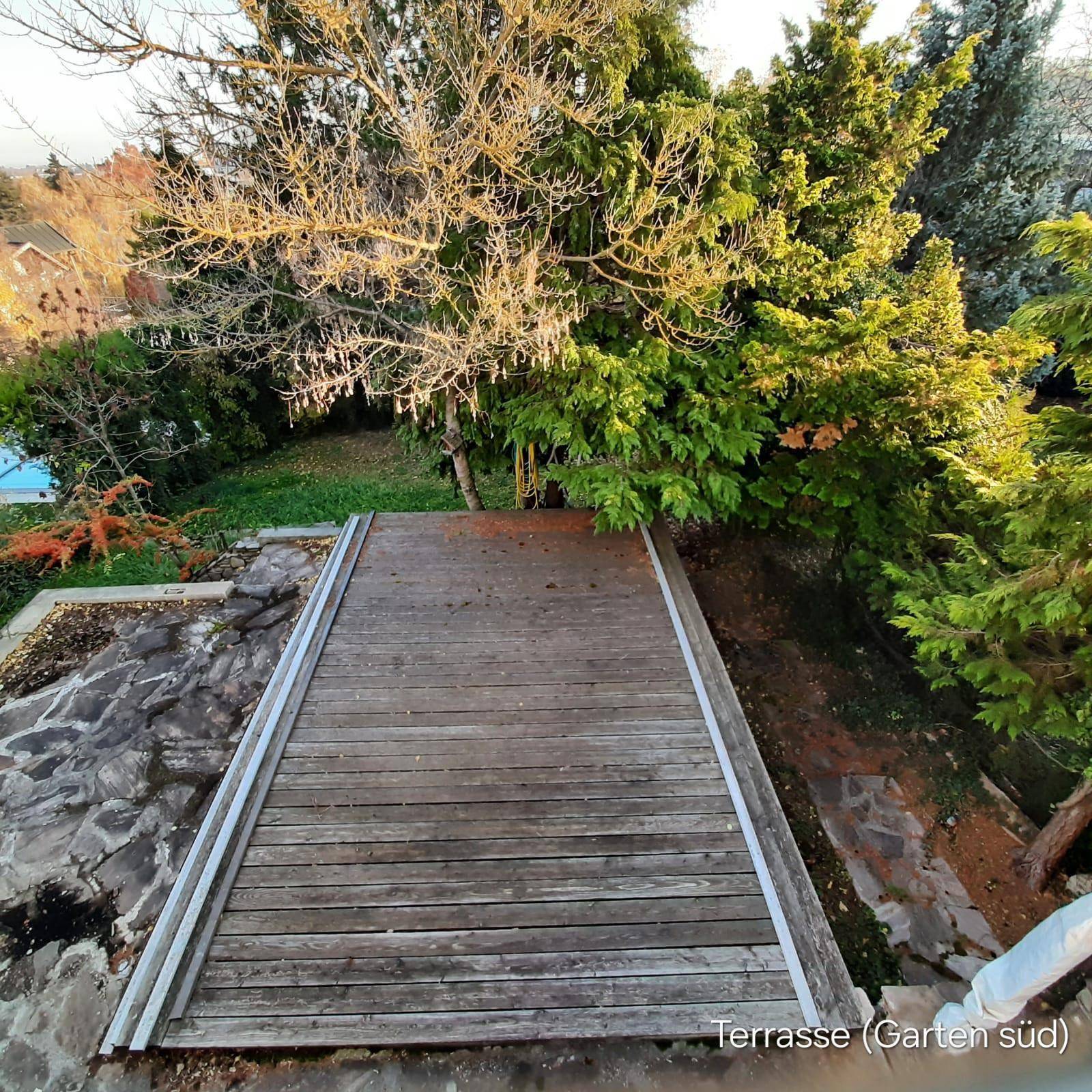 Hölzerne Terrasse im Gartenbereich, umgeben von üppigem Grün und Bäumen.