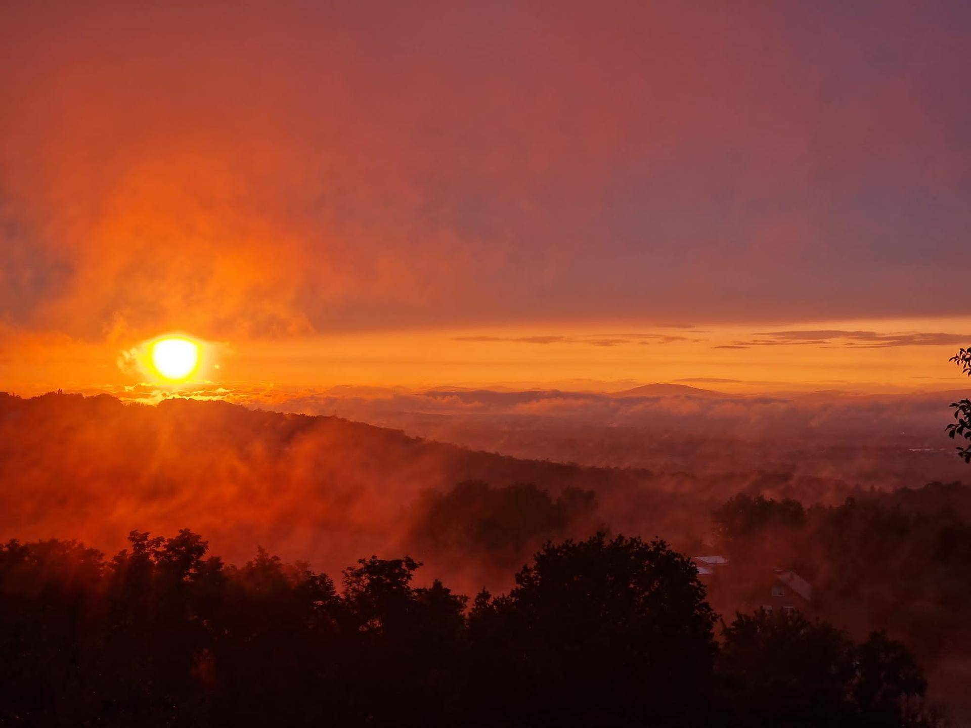 Atemberaubender Sonnenaufgang über einer nebligen Hügellandschaft mit leuchtenden Farben am Horizont.