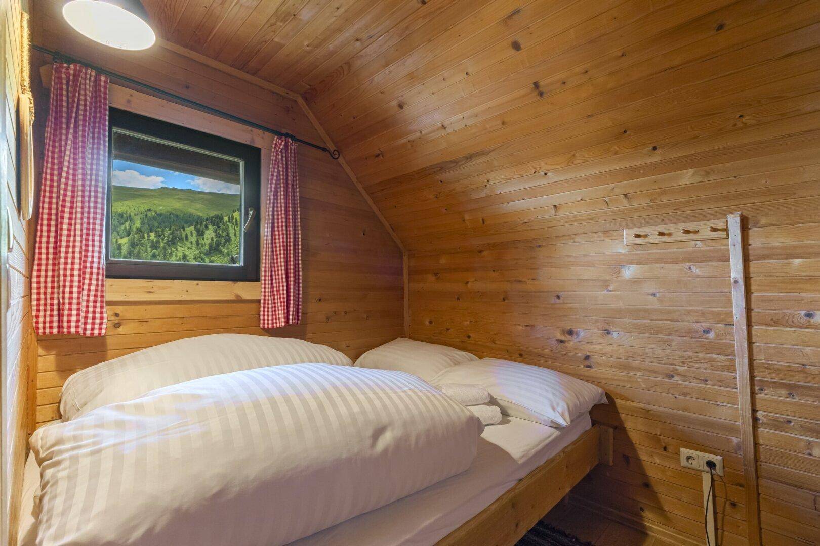 Helles Schlafzimmer mit Holztäfelung, Dachschräge und Fenster mit Blick auf die grüne Landschaft.