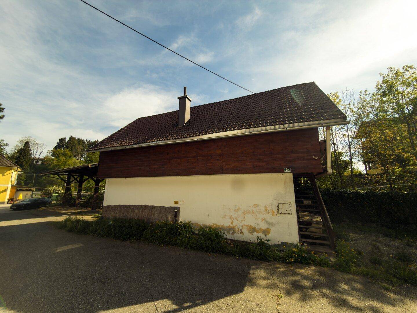 Seitenansicht eines Gebäudes mit Holzverkleidung und Satteldach in ländlicher Umgebung.