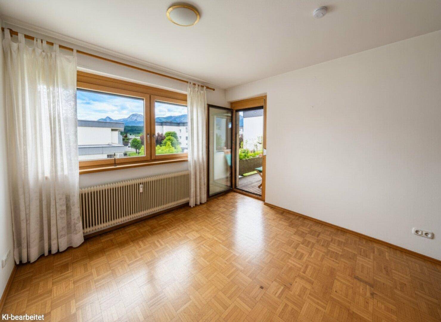 Schlafzimmer mit Parkettboden, viel Tageslicht und direktem Zugang zum Balkon mit Bergblick.