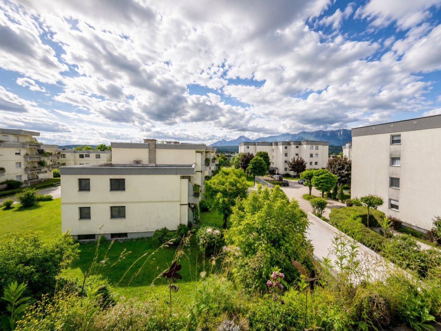 Weitläufige Wohnanlage mit viel Grün und Bergblick unter blauem Himmel.