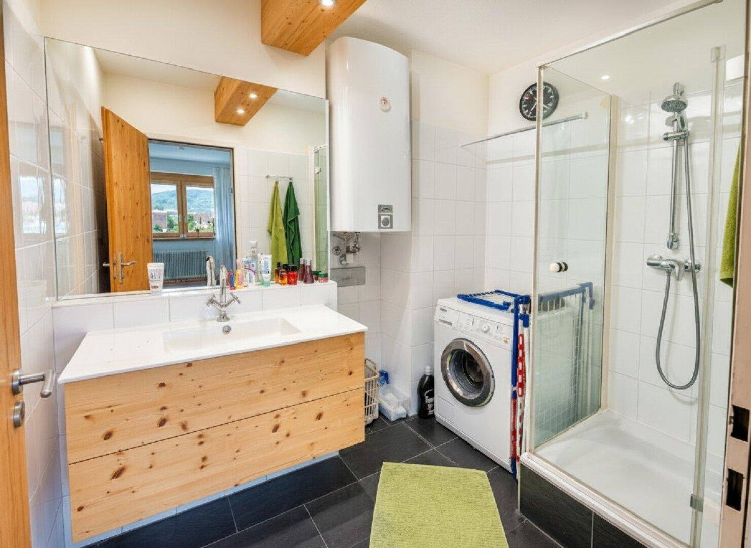 Modernisiertes Badezimmer mit Dusche, Waschbecken und Waschmaschinenanschluss.