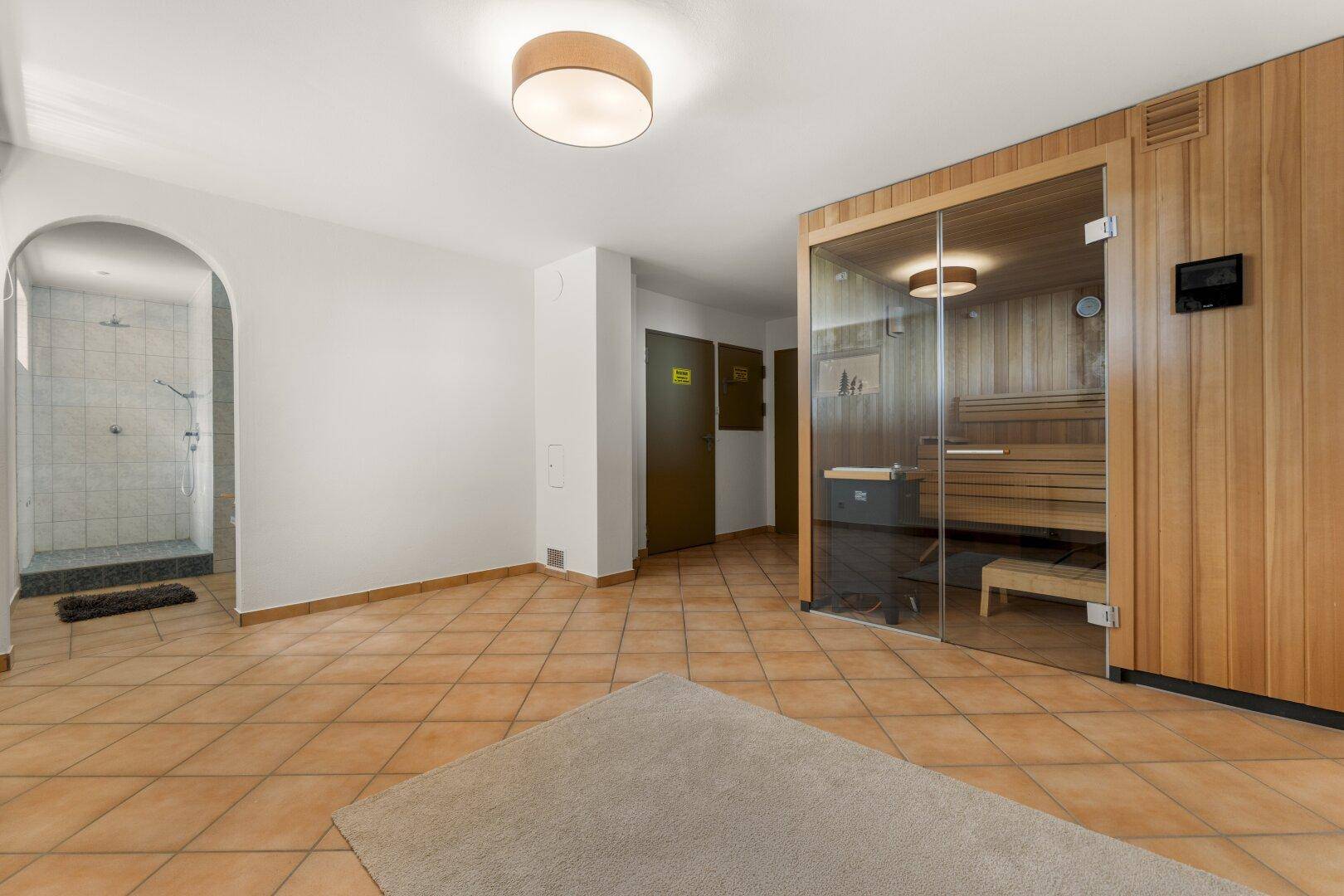 Entspannender Wellnessbereich mit moderner Sauna, separater Dusche und hellen Fliesenböden.