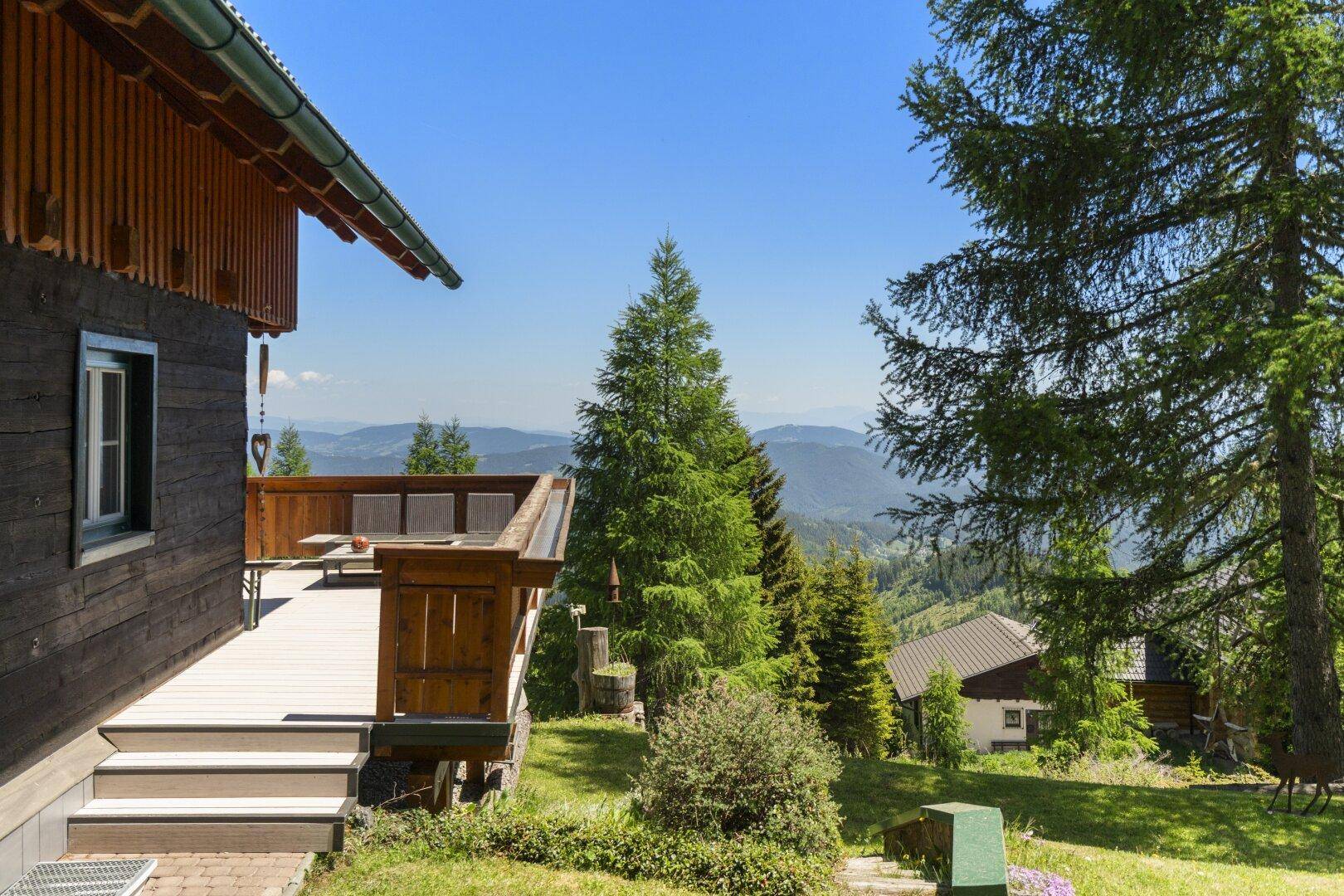 Seitenansicht des Hauses mit Terrasse, Treppe zum Garten und weitem Blick auf die bewaldete Berglandschaft.