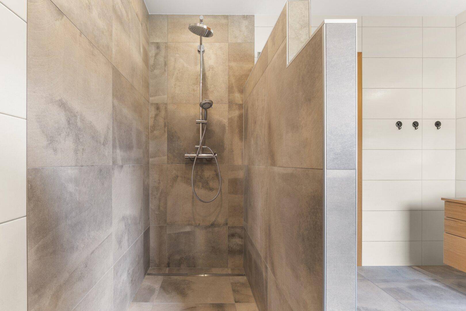 Geräumige, geflieste begehbare Dusche mit moderner Duscharmatur in neutralen Farbtönen.