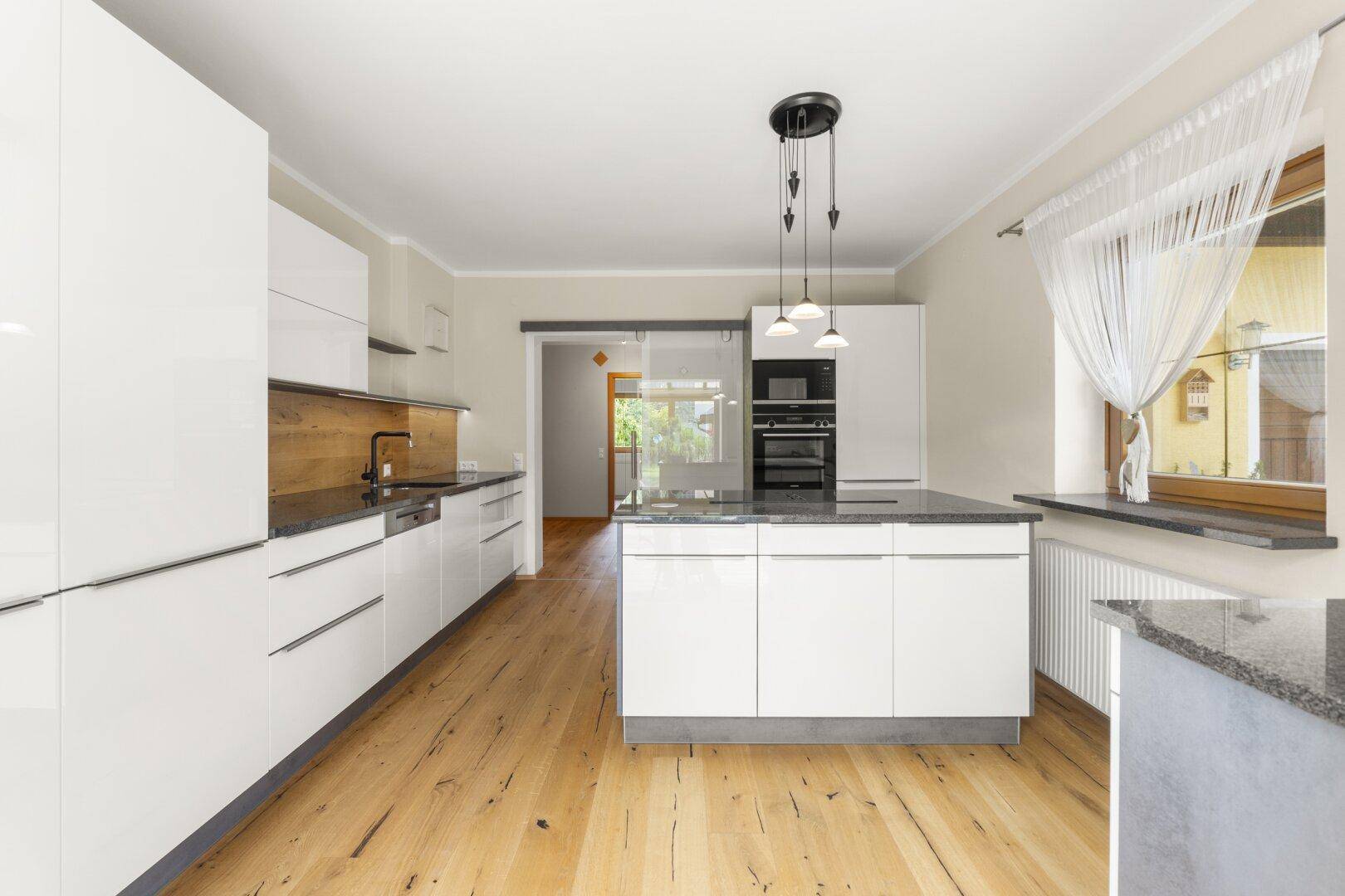 Moderne Küche mit weißen Hochglanzfronten, Kücheninsel und dunkler Granitarbeitsplatte, mit Holzboden.