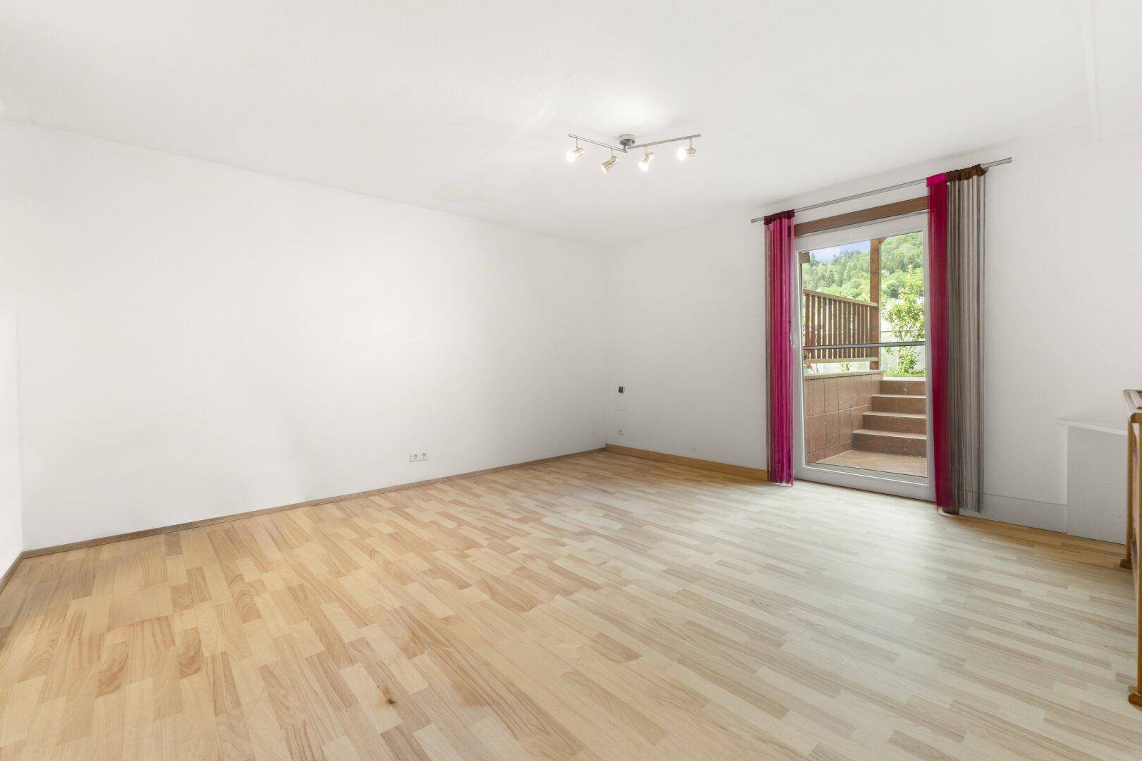 Helles Zimmer mit Holzboden und Zugang zu einer Außenterrasse über eine kleine Treppe.