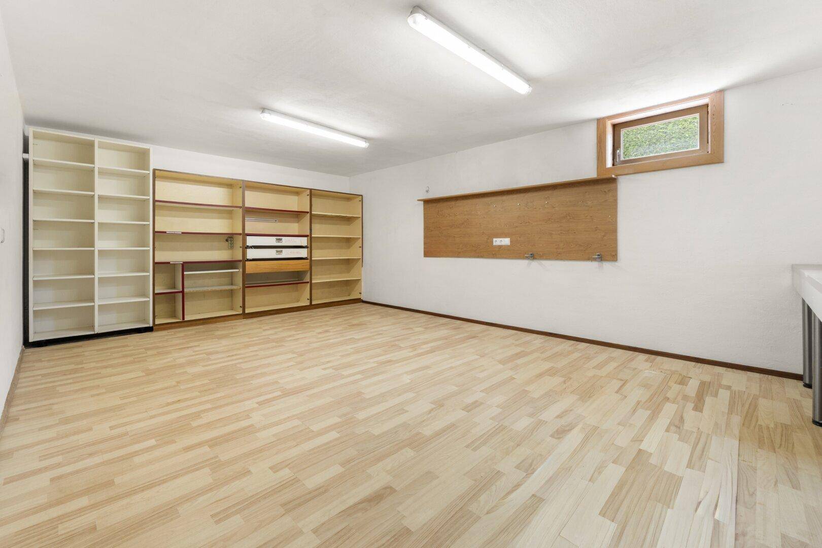 Praktischer Kellerraum mit Regalen, kleinem Fenster und Laminatboden, ideal als Abstellfläche.