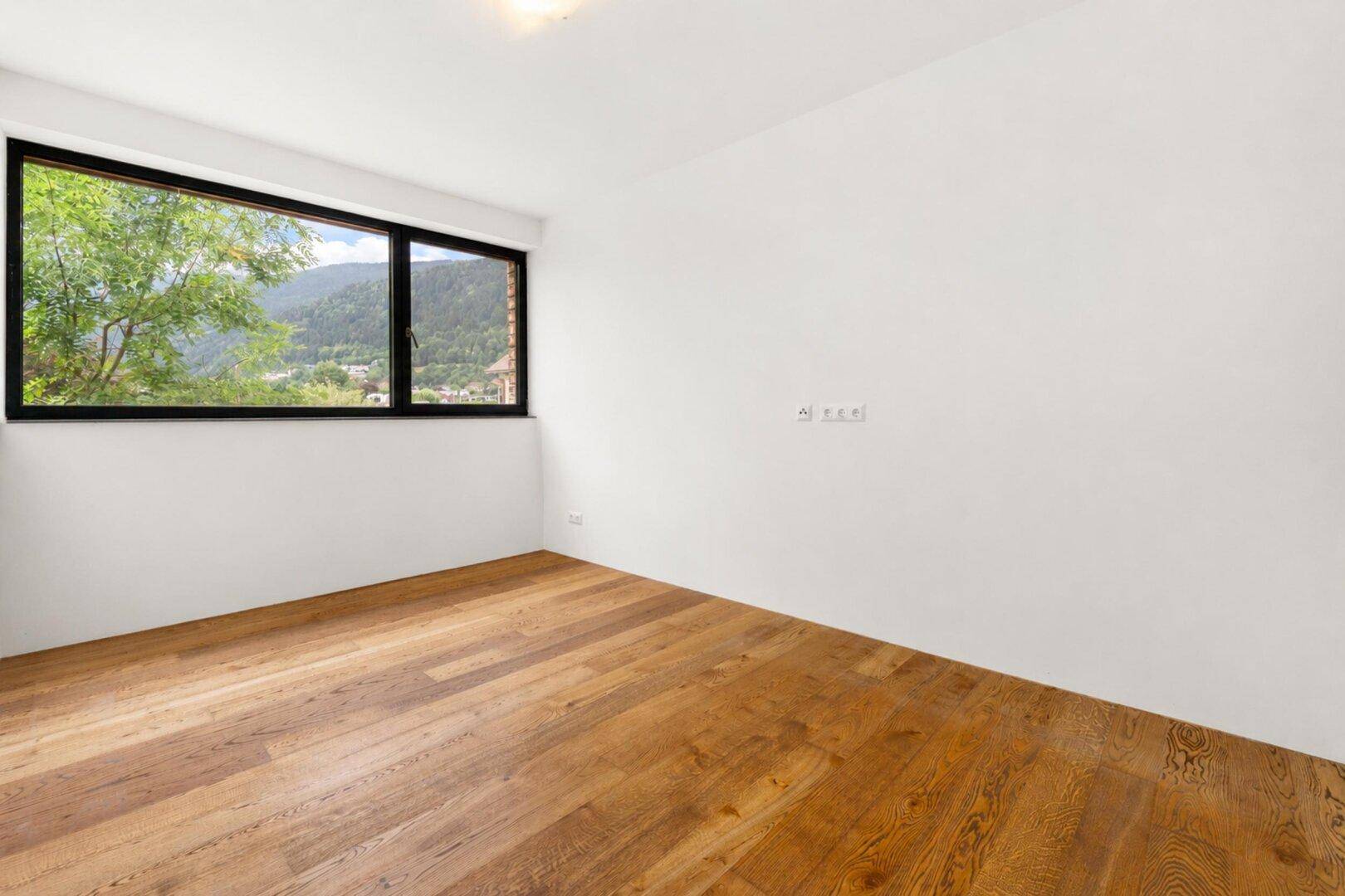 Helles Zimmer mit Holzboden und Fenster mit Blick auf die umliegende Landschaft.