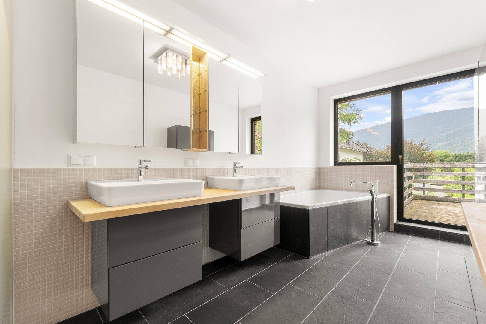 Modernes Badezimmer mit Doppelwaschbecken, Badewanne und Balkonzugang.