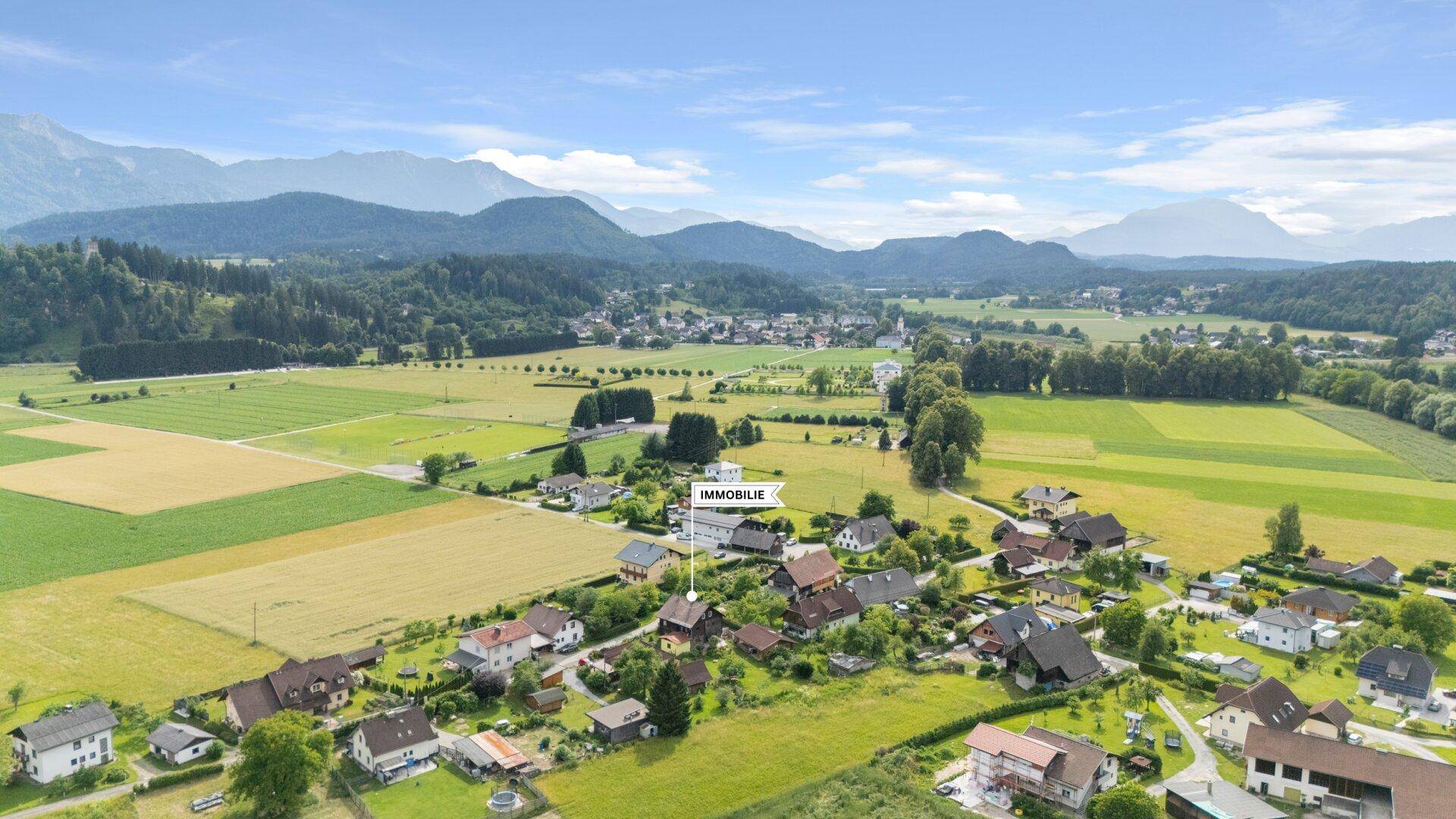 Luftaufnahme der ländlichen Umgebung mit Bergen, grünen Feldern und Siedlung.