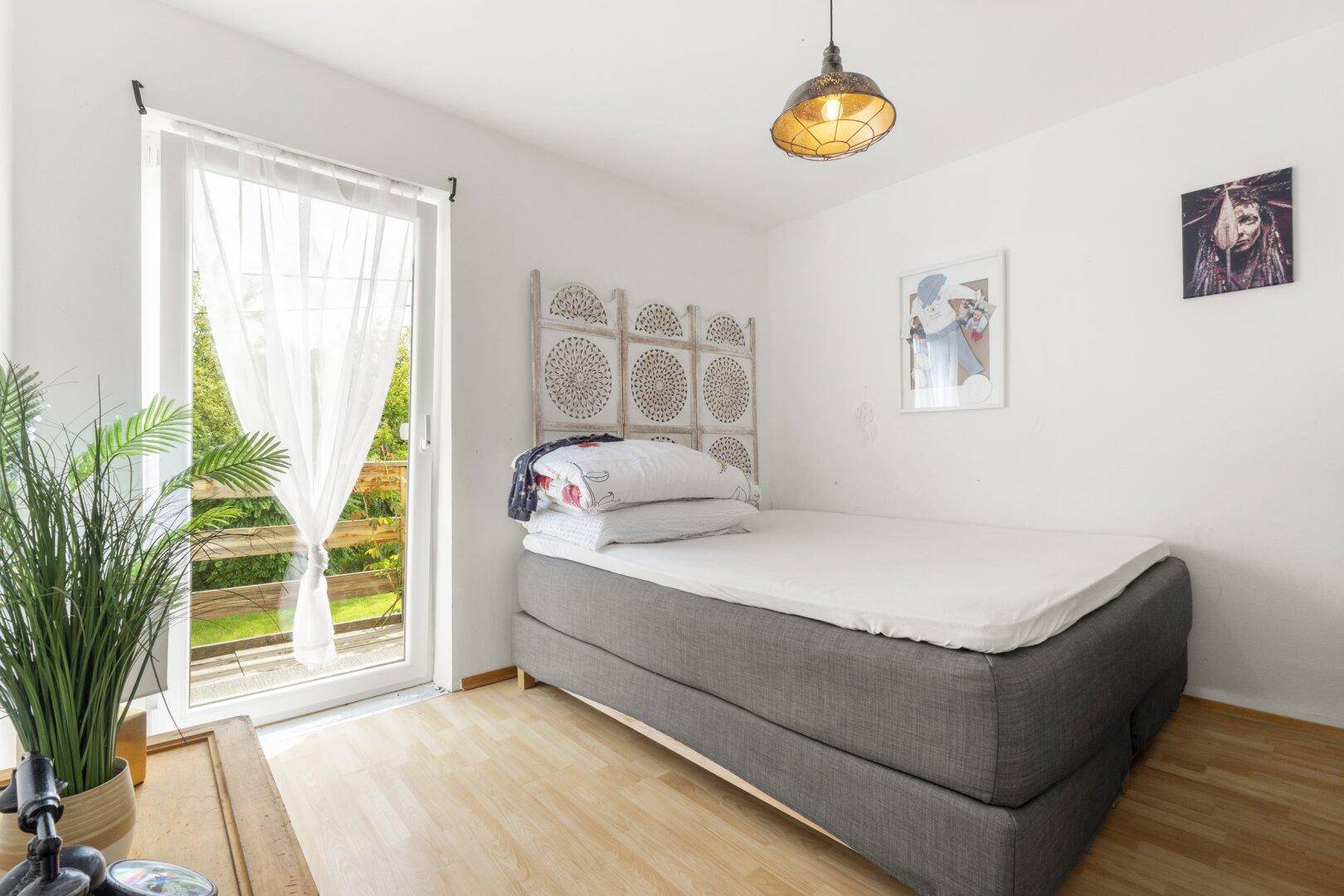 Schlafzimmer mit Balkonzugang, Holzboden und viel Tageslicht.