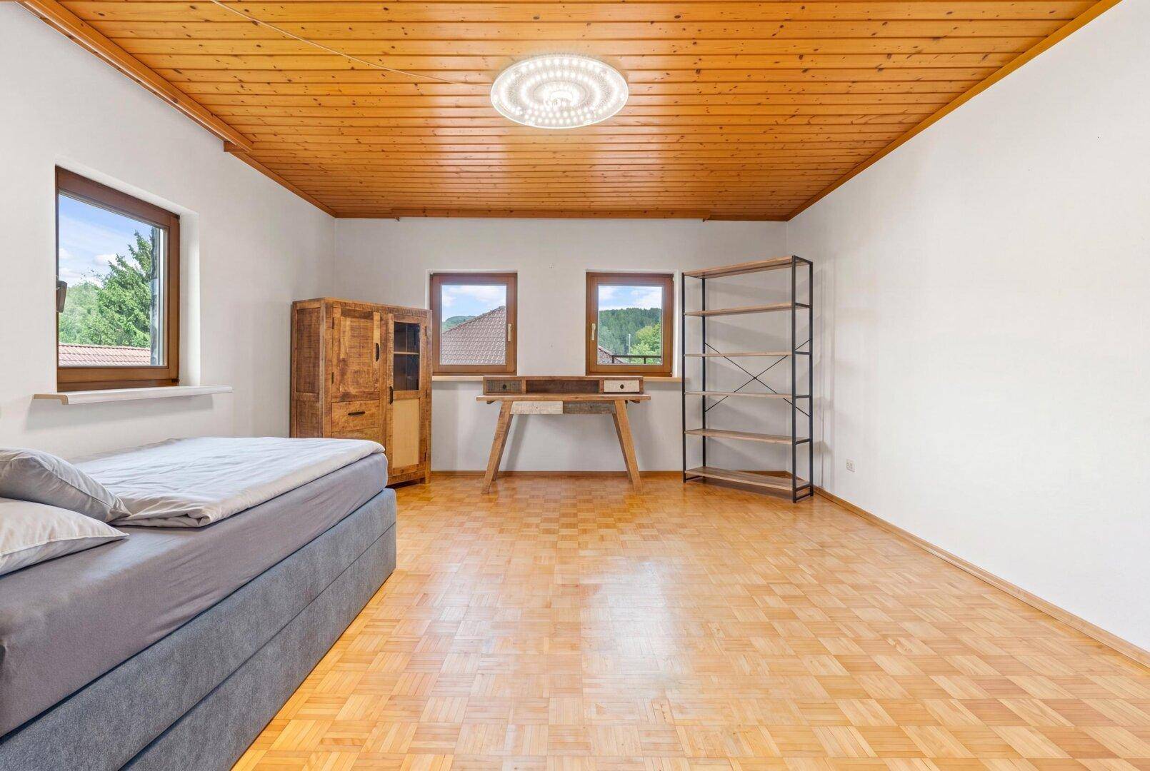 Helles Schlafzimmer mit Holzdecke, Parkettboden und Blick ins Grüne.