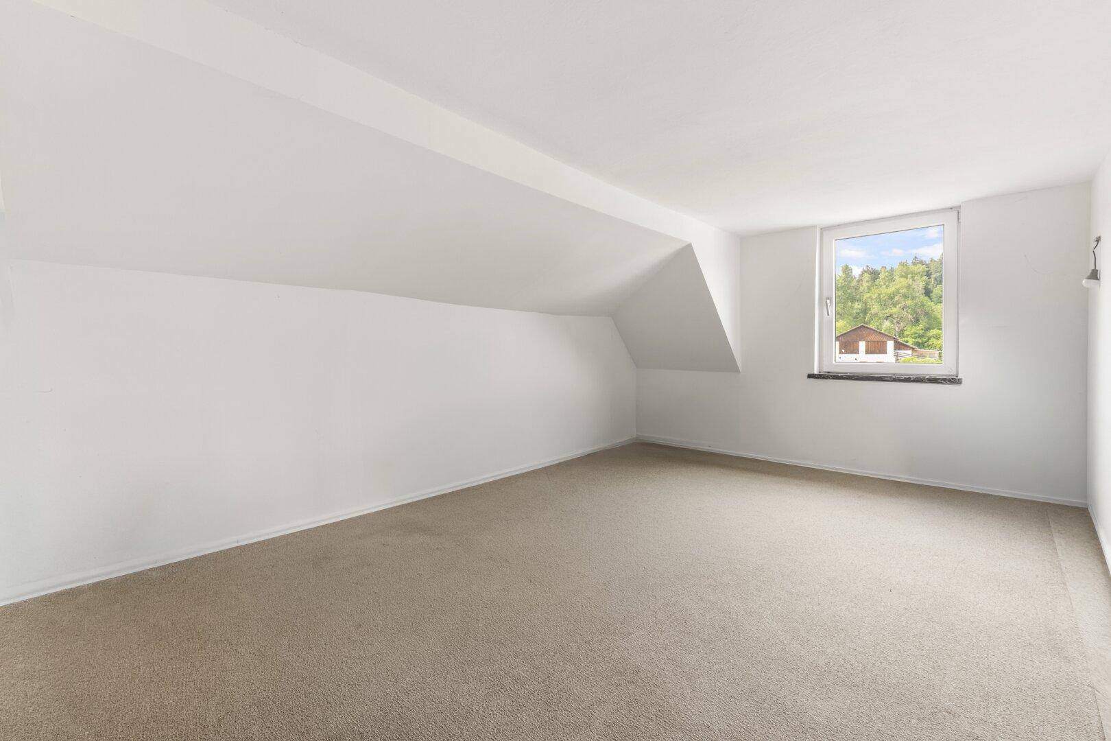 Geräumiger Dachbodenraum mit Teppichboden und Dachschräge.