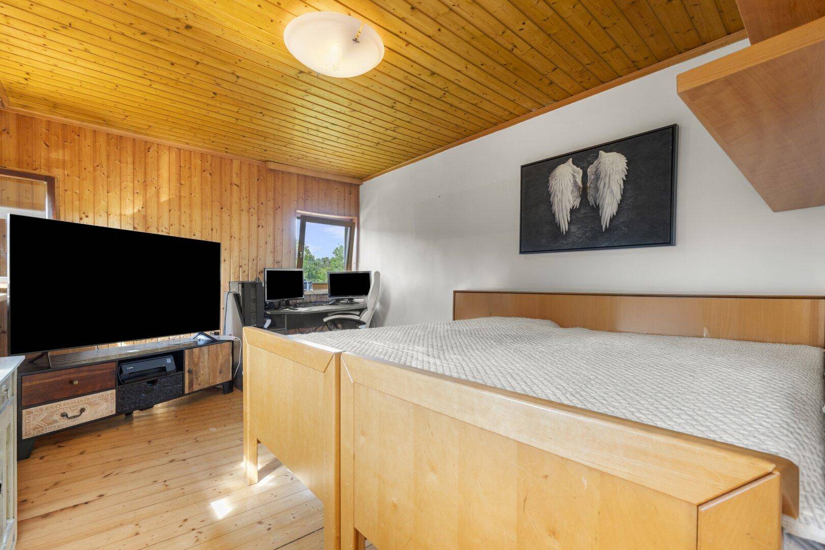 Gemütliches Schlafzimmer mit Holzdecke, Holzboden und Arbeitsbereich.