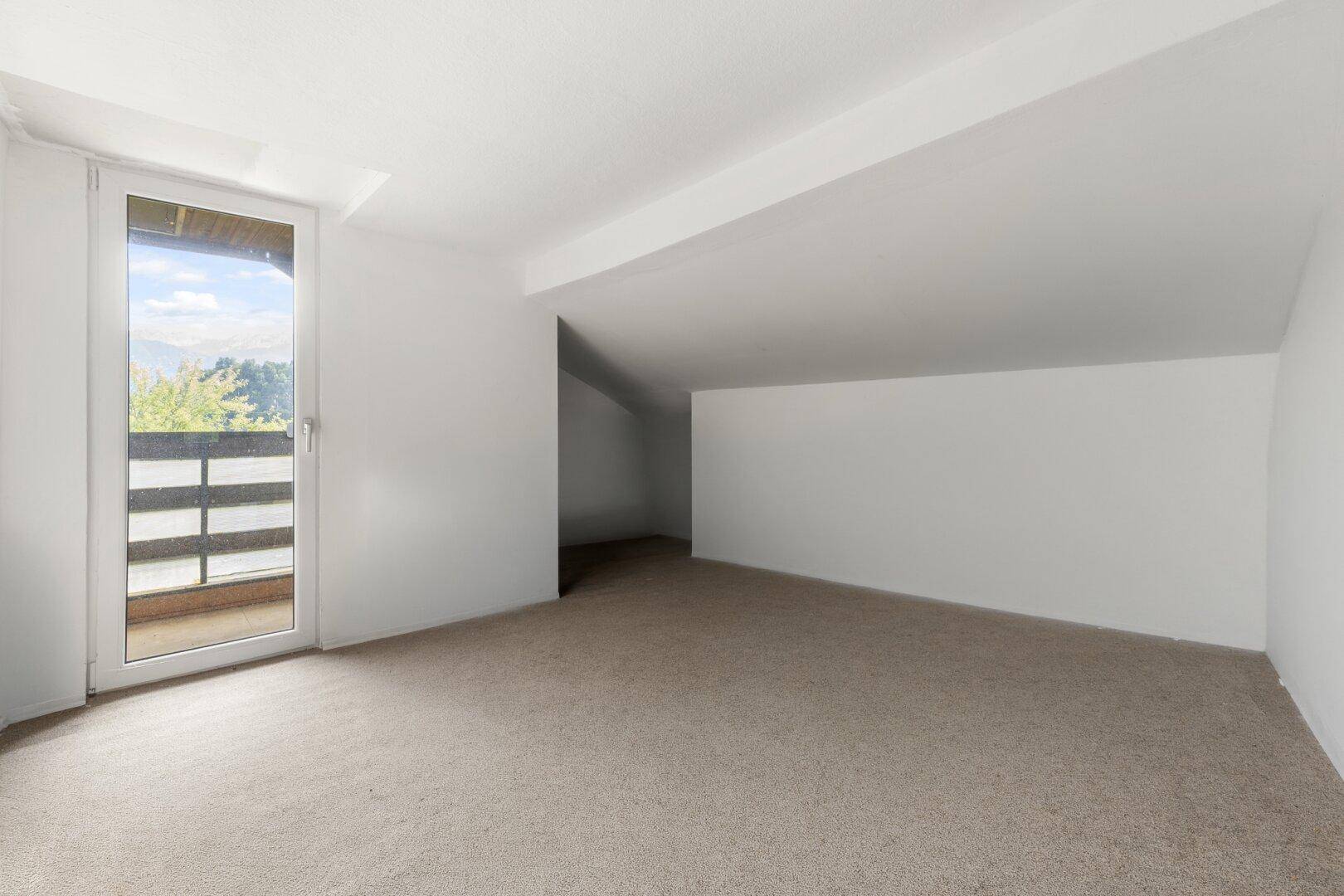 Dachbodenraum mit Balkonzugang, Teppichboden und viel Tageslicht.