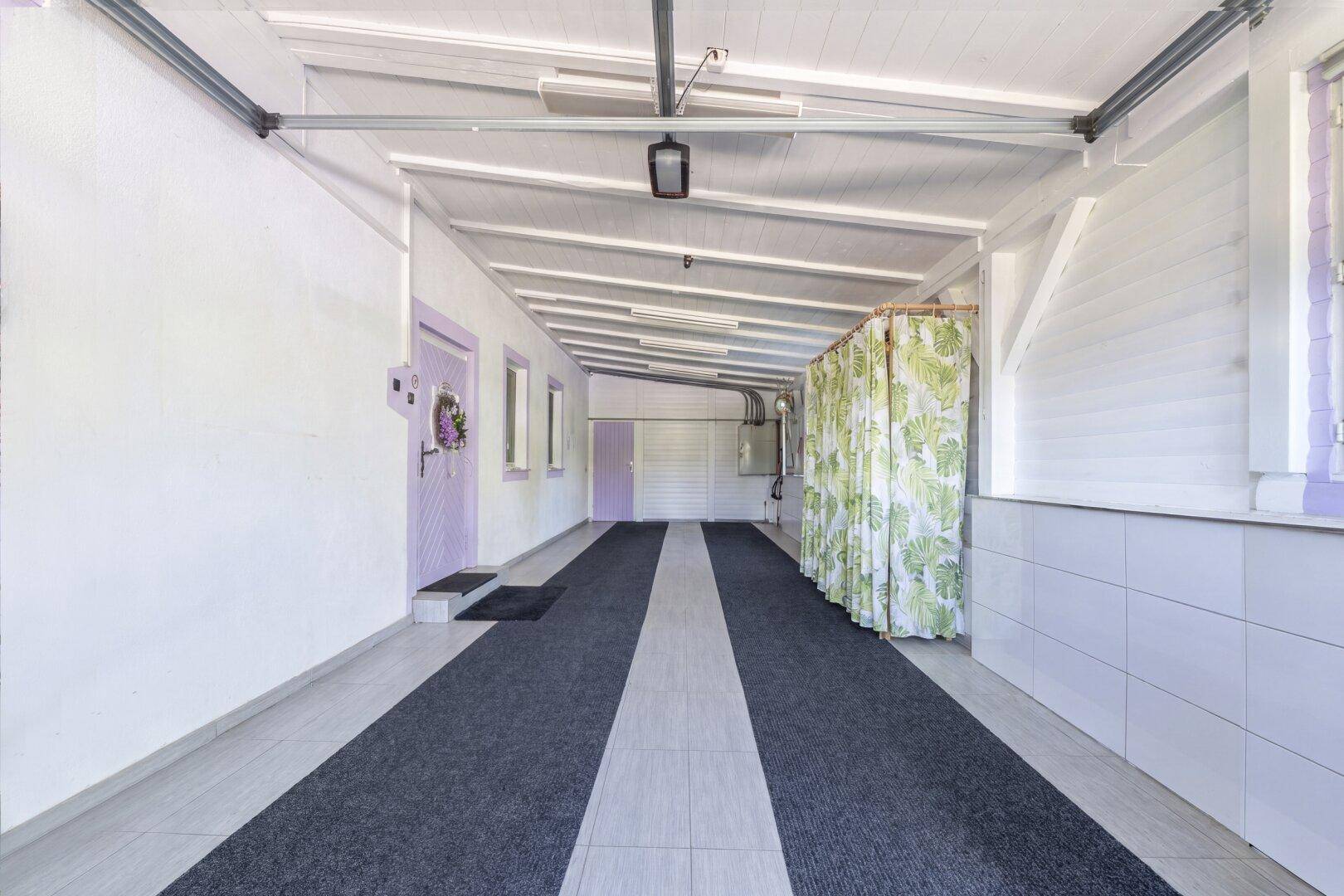 Überdachter Einfahrtsbereich mit Fliesenboden, der als Carport oder Mehrzweckraum dient.