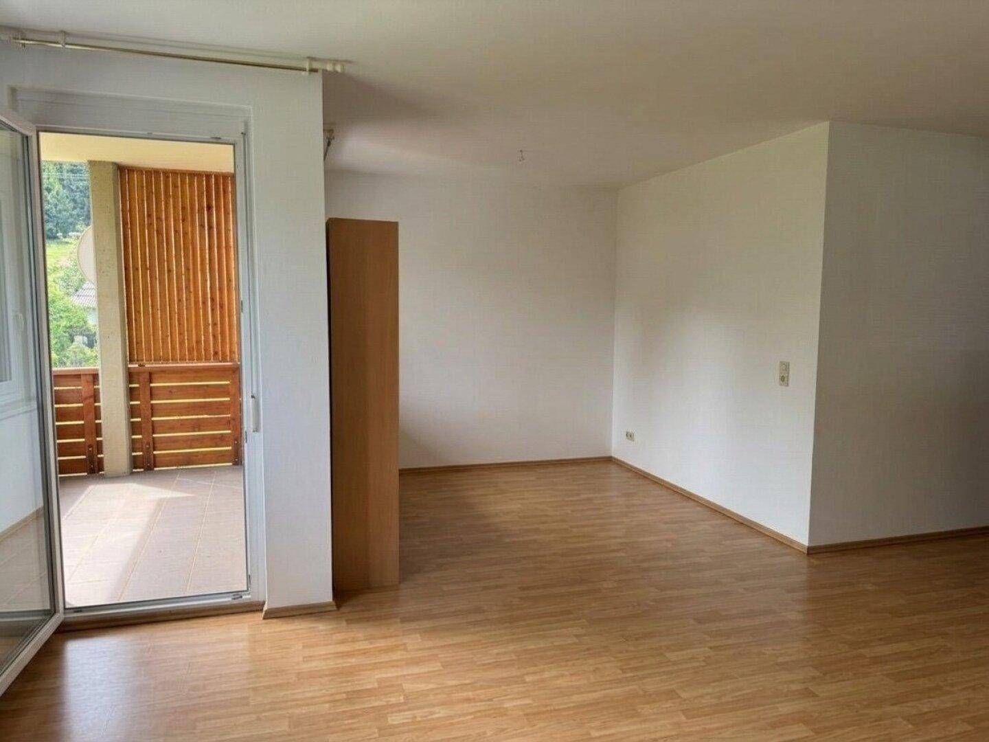 Leeres Wohnzimmer mit Laminatboden, weißen Wänden und direktem Zugang zum Balkon.