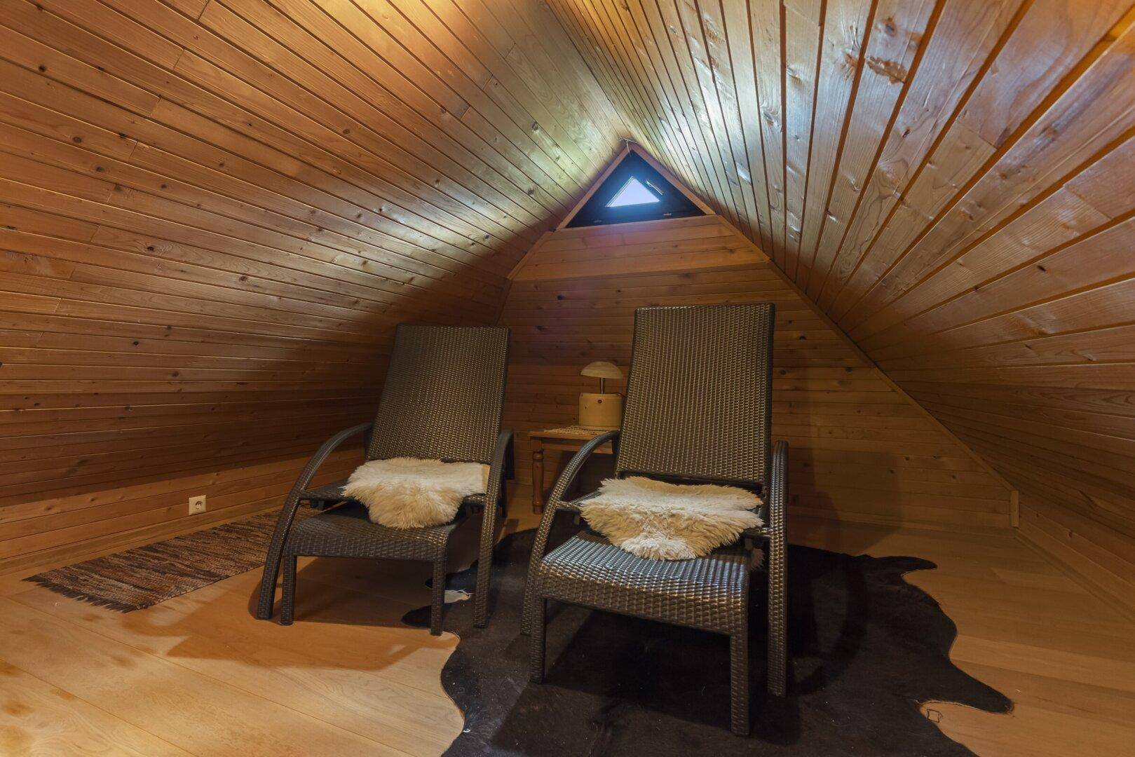 Entspannungsbereich im Dachgeschoss mit Holztäfelung, bequemen Liegestühlen und kleinem Dachfenster.