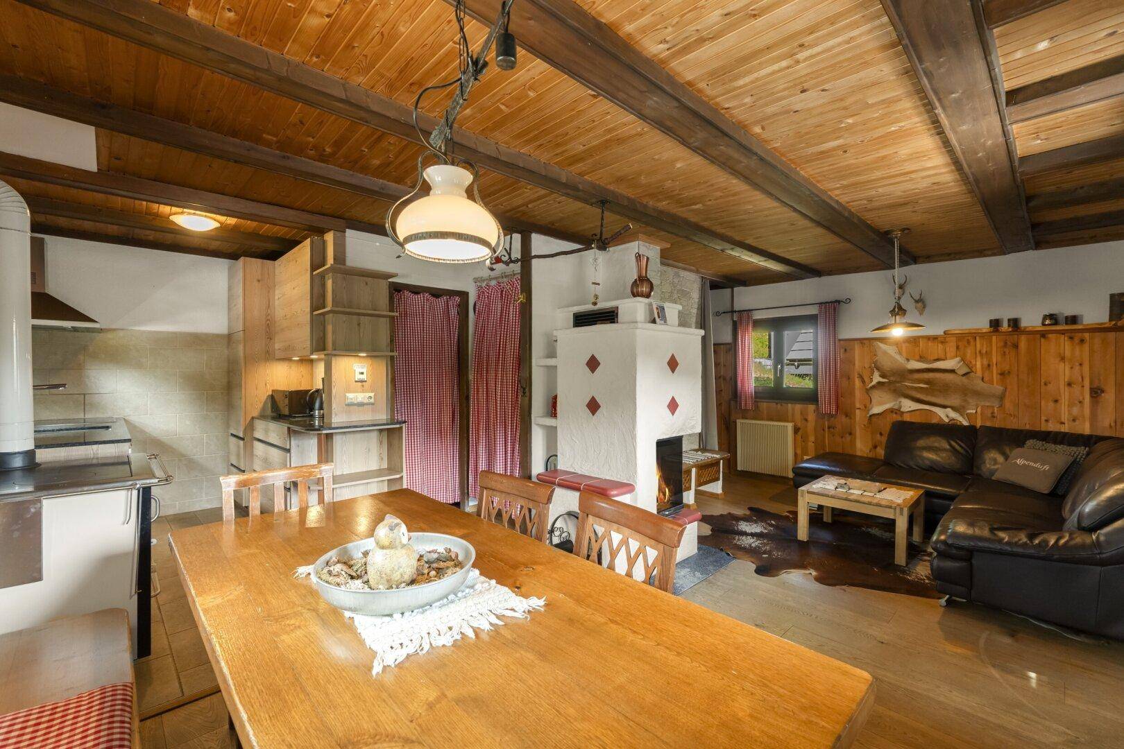 Gemütlicher Wohn-Essbereich mit Holzbalkendecke, Kachelofen und integrierter Küche im alpinen Stil.
