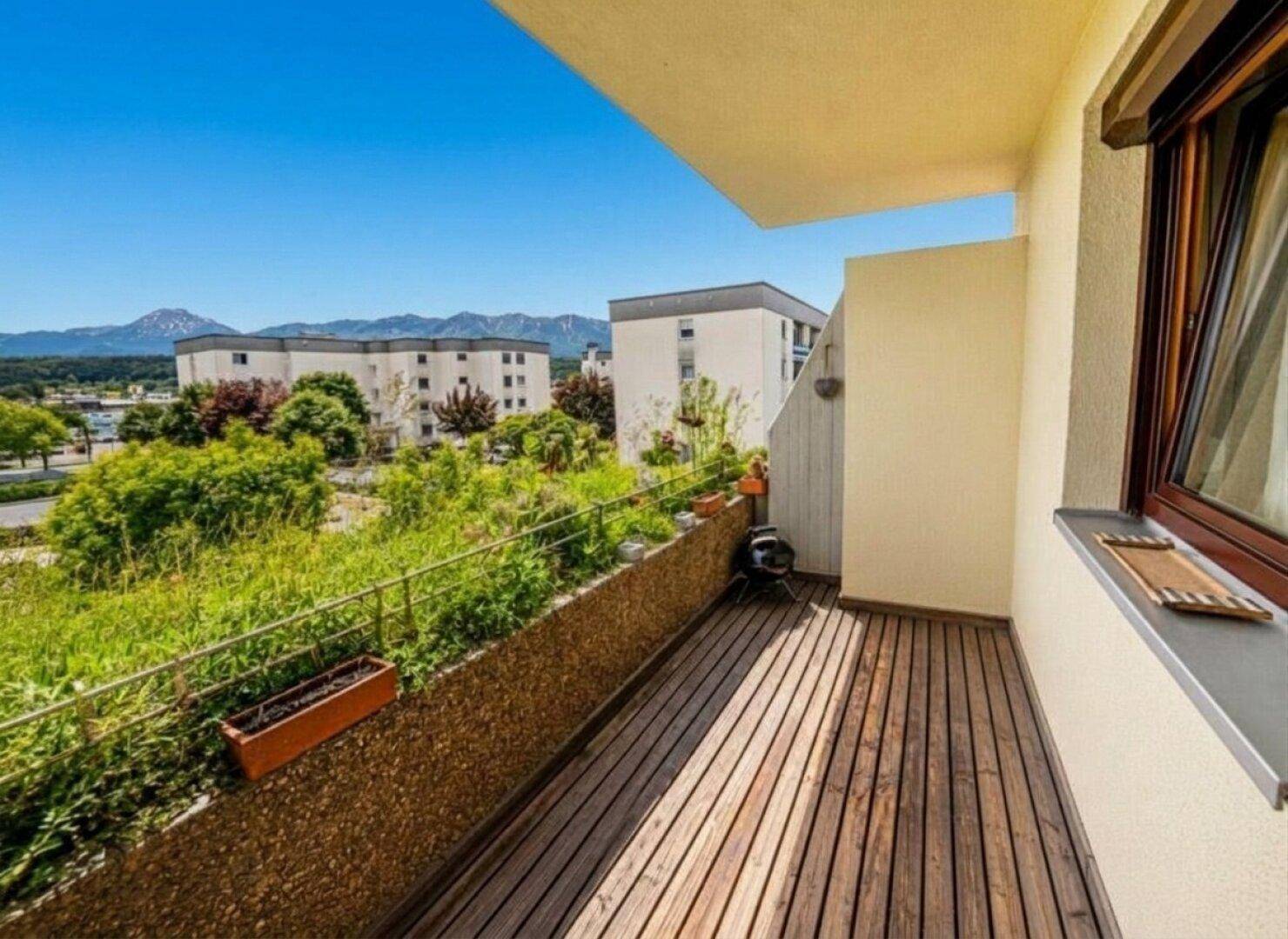 Sonniger Balkon mit Holzboden, Pflanzen und weitem Blick auf die umliegende Berglandschaft.
