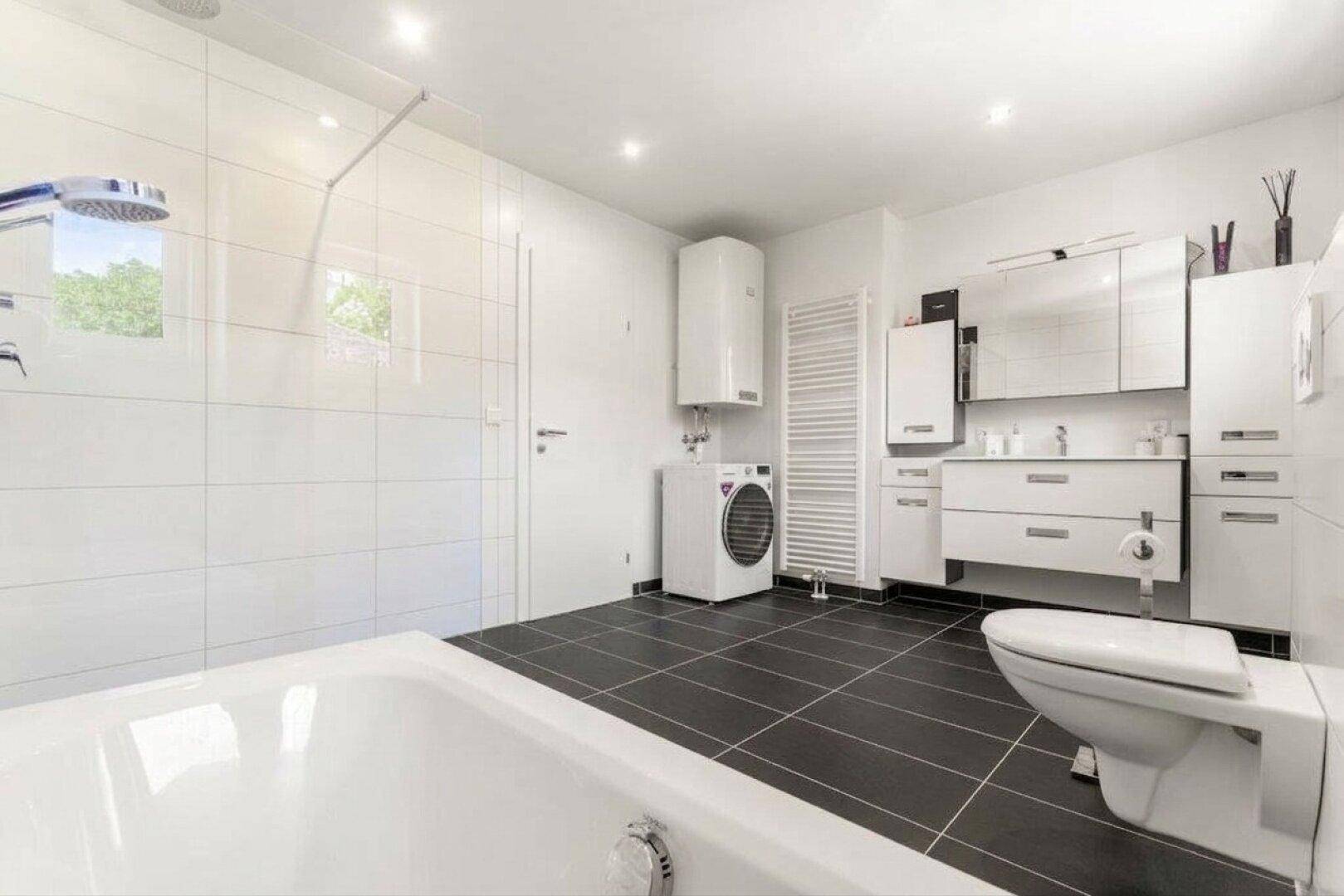 Modernes Badezimmer mit Badewanne, begehbarer Dusche, Doppelwaschbecken und Waschmaschine.