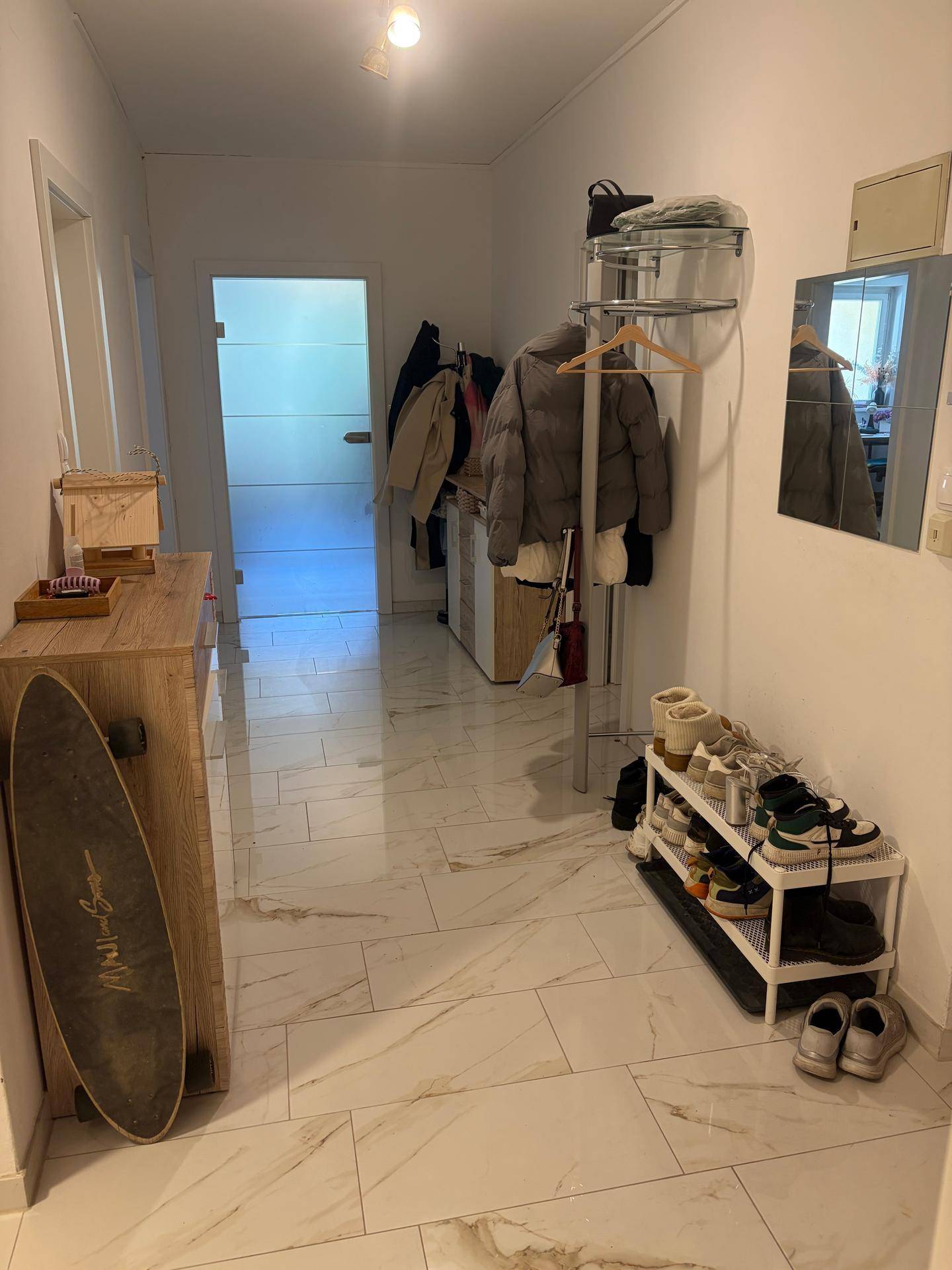Heller Flur mit glänzenden Marmorfliesen, Garderobe und Schuhregal, führt zu weiteren Räumen.