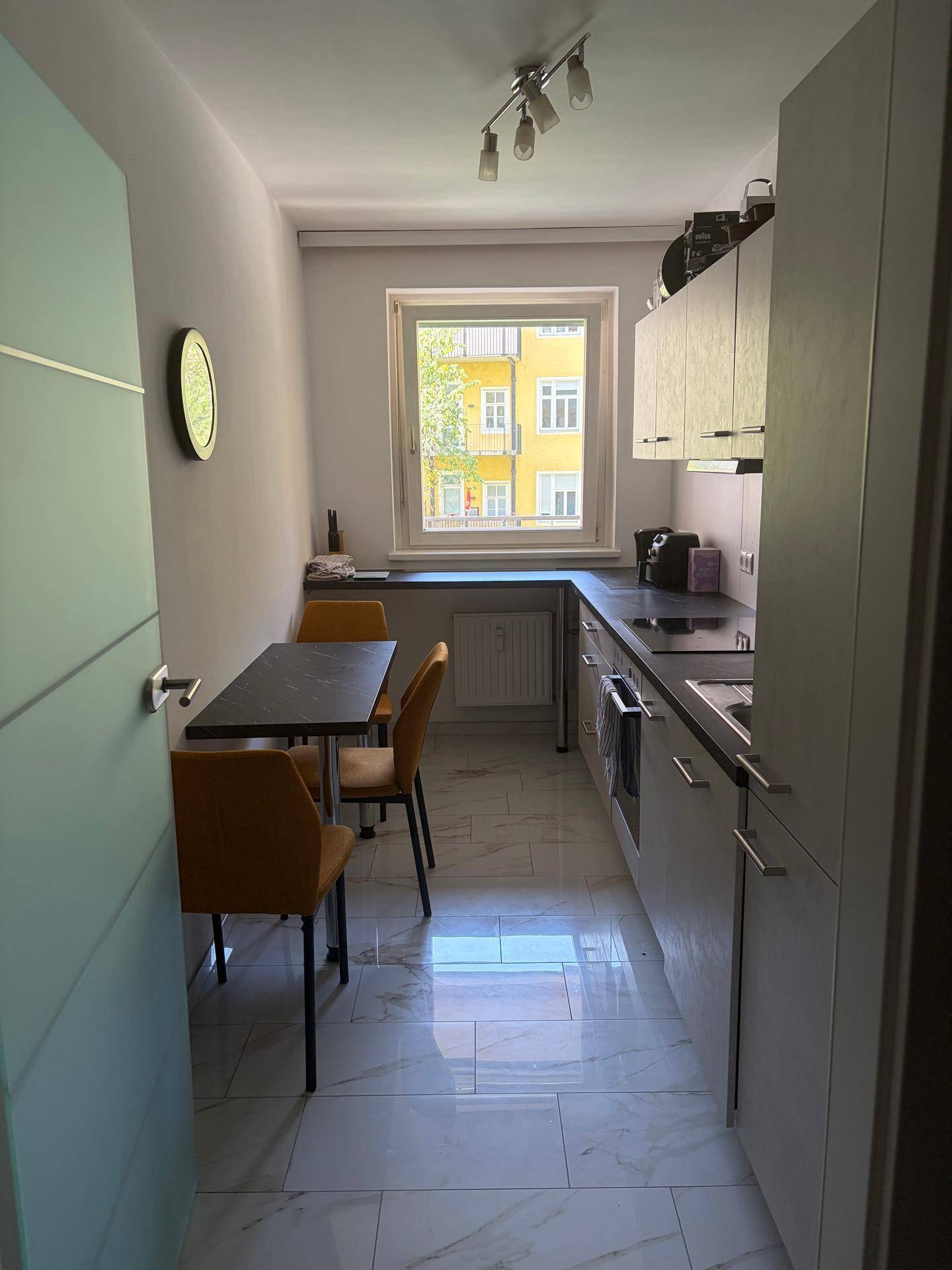 Funktionale Küche mit grauen Schränken, Essbereich und Fenster, ausgestattet mit modernen Geräten.