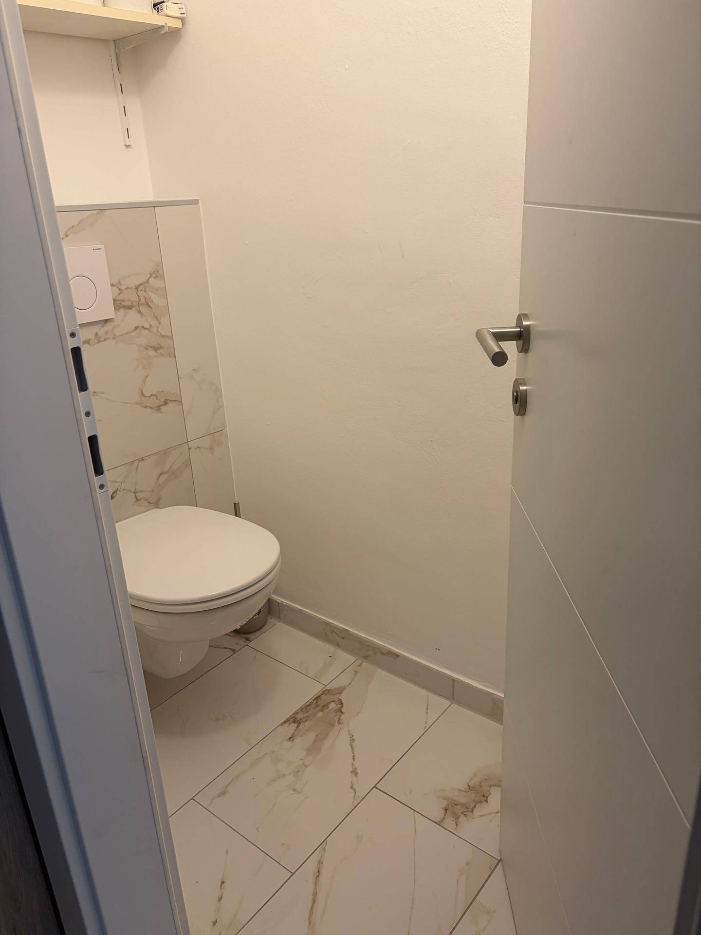 Kleines Gäste-WC mit wandhängender Toilette und hellen Fliesen an Wänden und Boden.
