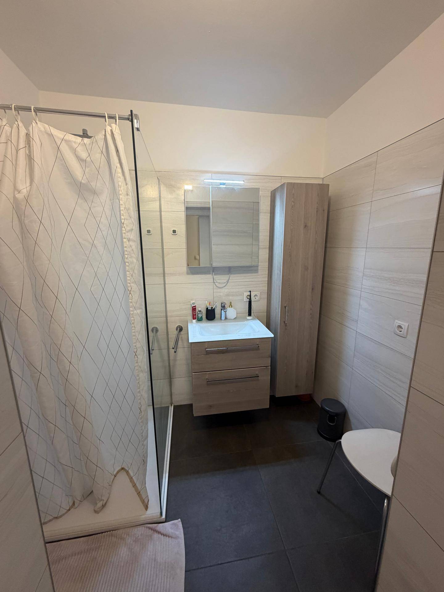 Modernes Badezimmer mit ebenerdiger Dusche, Einzelwaschbecken und Spiegelschrank.
