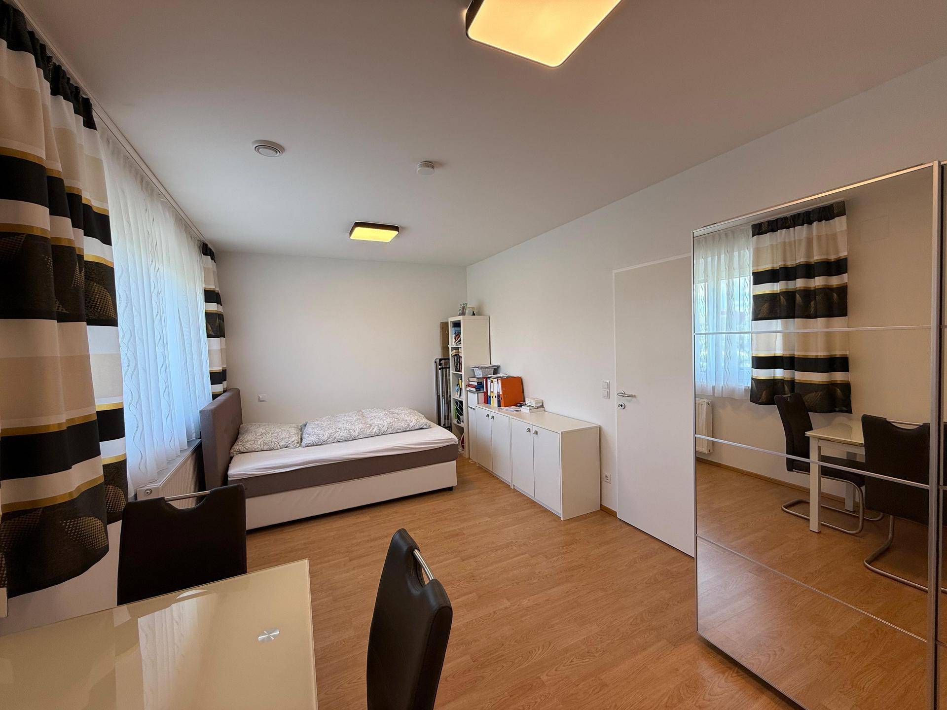 Schlafzimmer mit Einzelbett, Spiegelschrank und Holzboden, hell und funktional eingerichtet.
