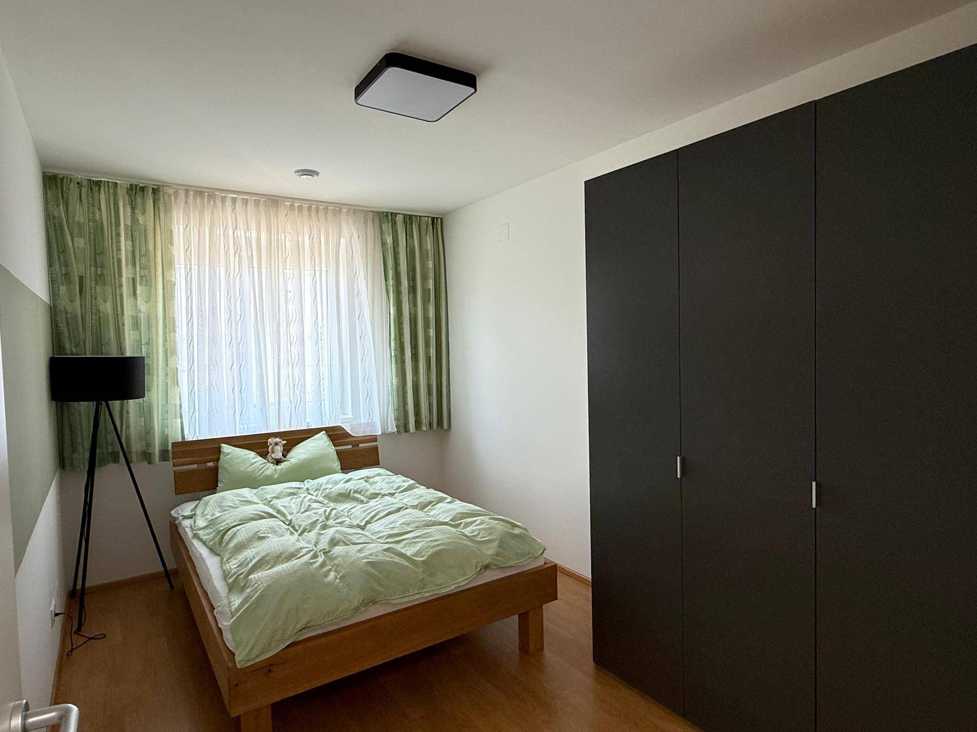 Gemütliches Schlafzimmer mit Holzbett, grünem Bettzeug und dunklem Kleiderschrank, gut beleuchtet.