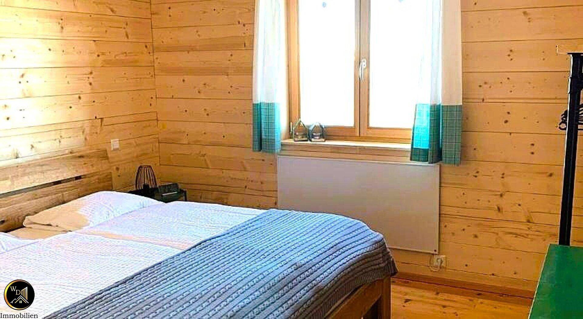 Helles Schlafzimmer mit Holzwänden, Doppelbett und Fenster mit Blick ins Grüne.