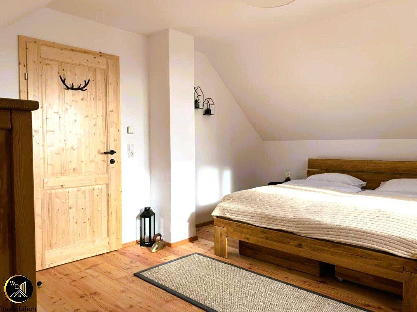 Schlafzimmer mit Holzbett, Holztür und Dachschräge.