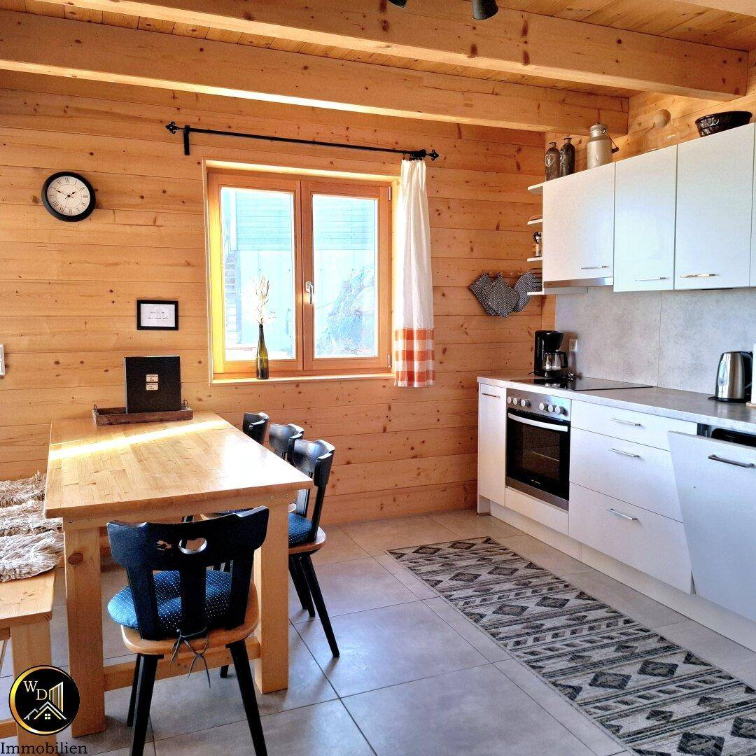 Moderne Küche mit weißen Schränken, Holzwänden und Essbereich am Fenster.