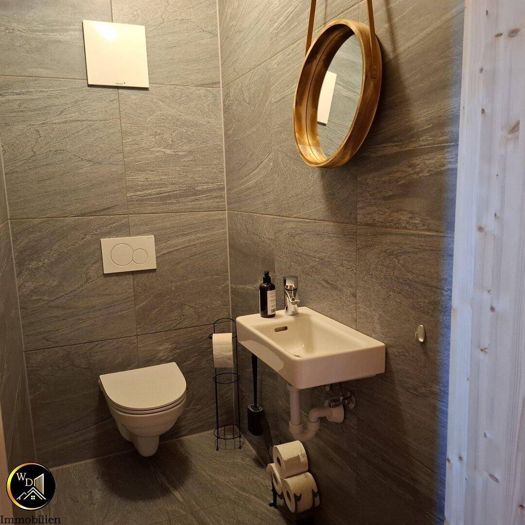 Modernes Gäste-WC mit Wand-WC, kleinem Waschbecken und grauen Fliesen.