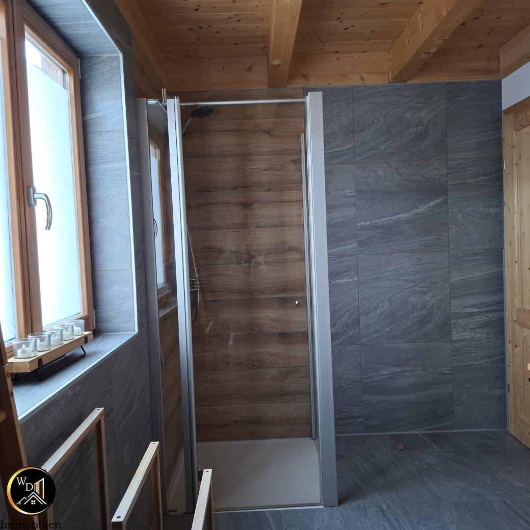Geräumige Dusche im modernen Badezimmer mit grauen Wand- und Bodenfliesen.